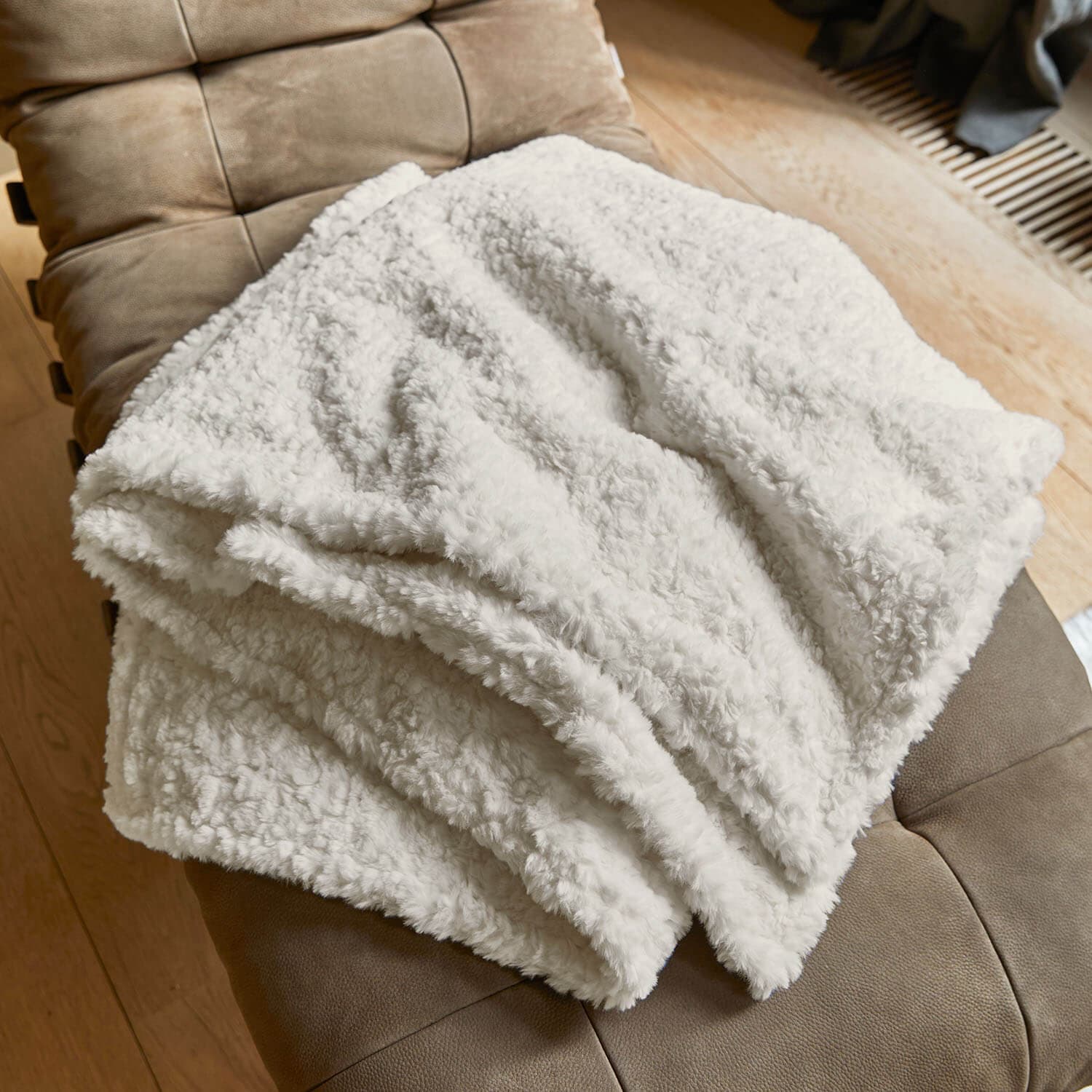 Manta blanca suave de material peludo sobre sillón marrón, perfecta para salón y descanso