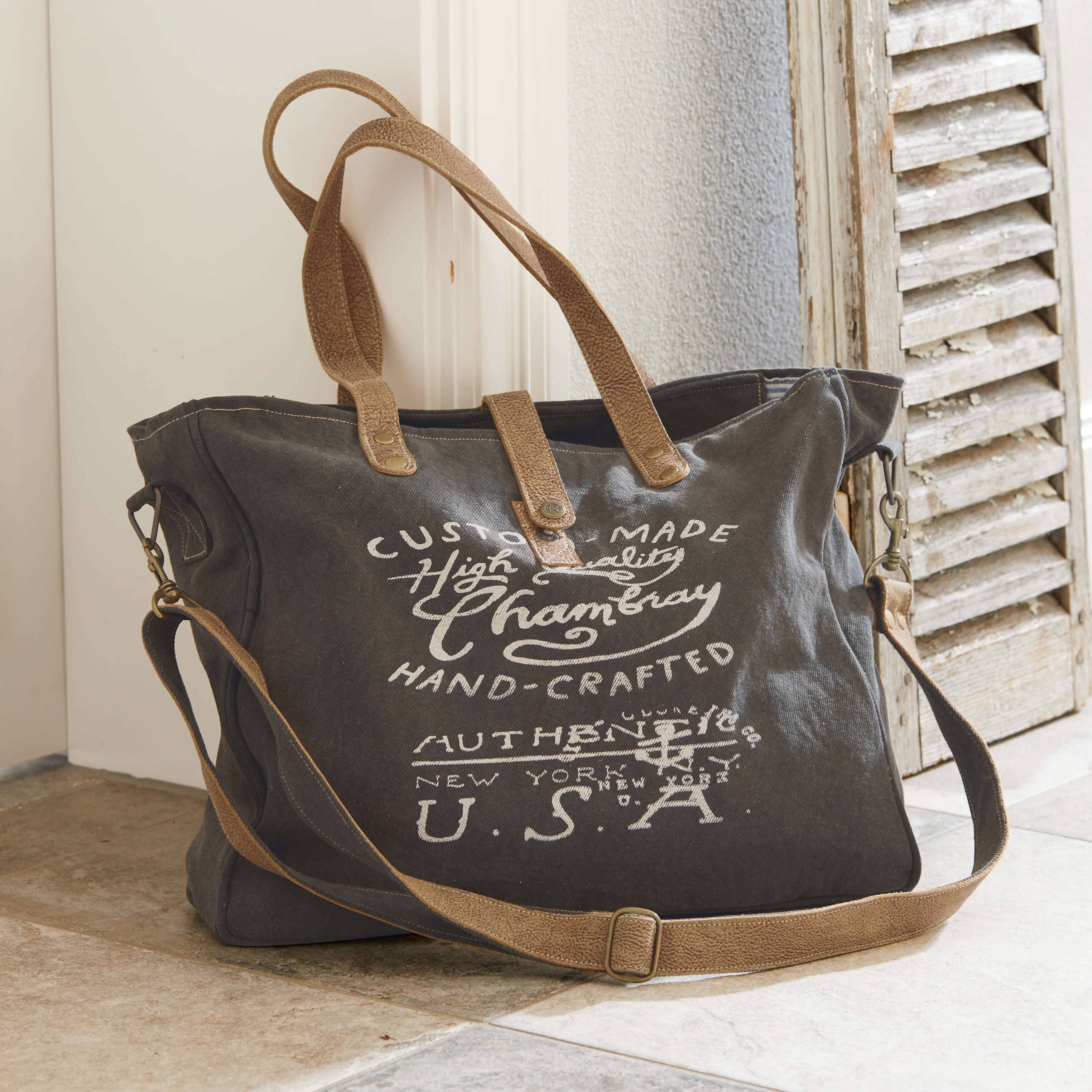 Bolsa de tela gris oscuro con asas de cuero marrón y texto impreso, bolsa de viaje