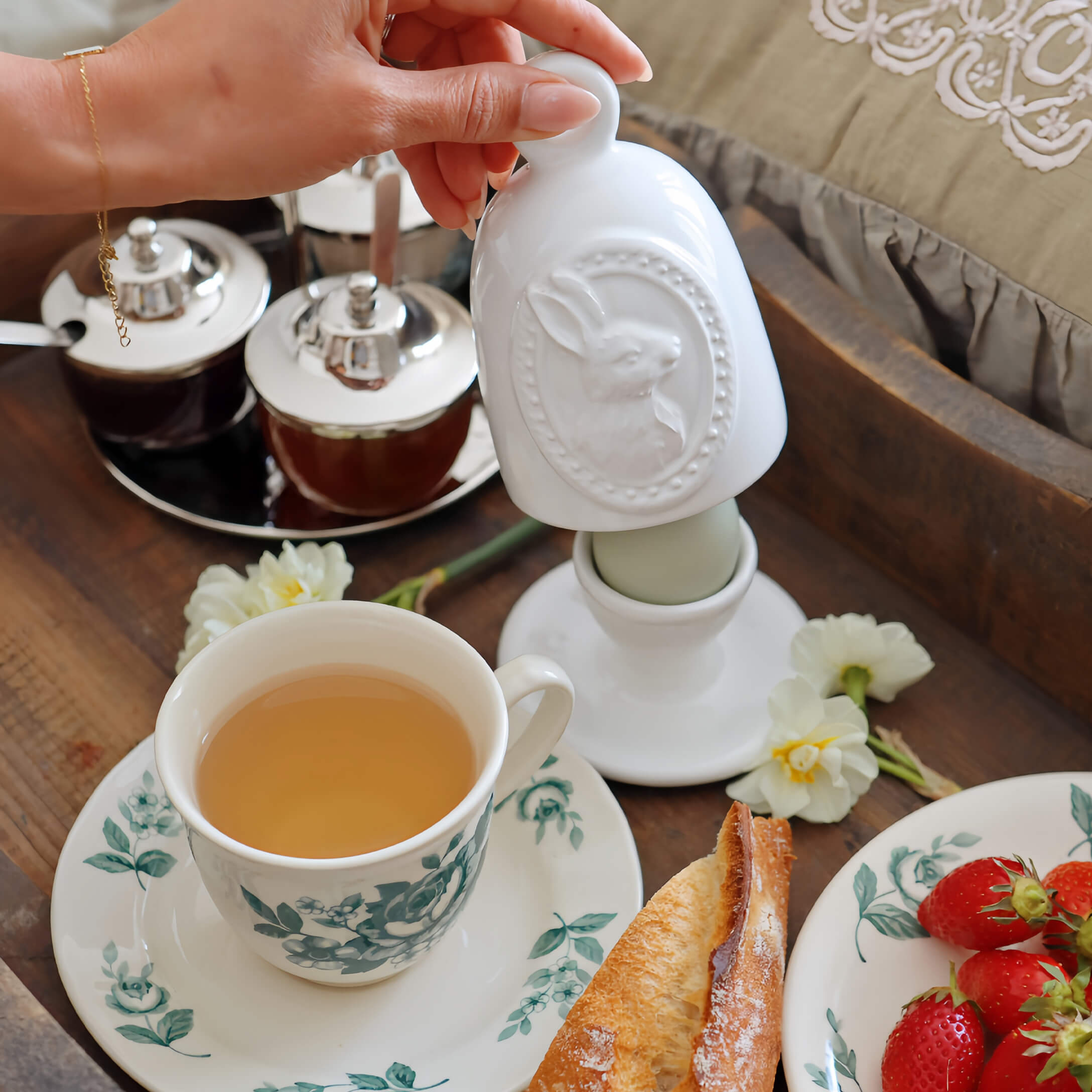 Recipiente de cerámica blanca con diseño de conejo en mesa de desayuno con té y fresas