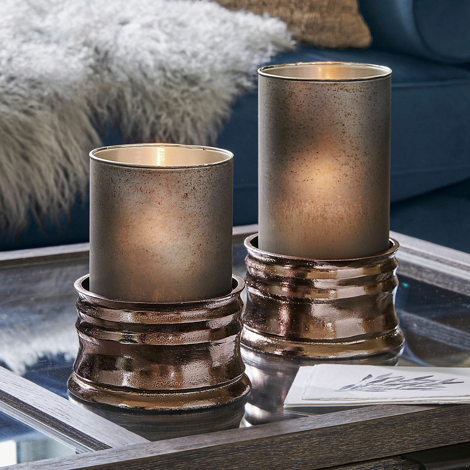 Set de 2 portavelas Eirun Dos portavelas decorativos de vidrio y metal cobre sobre mesa de cristal en salón moderno