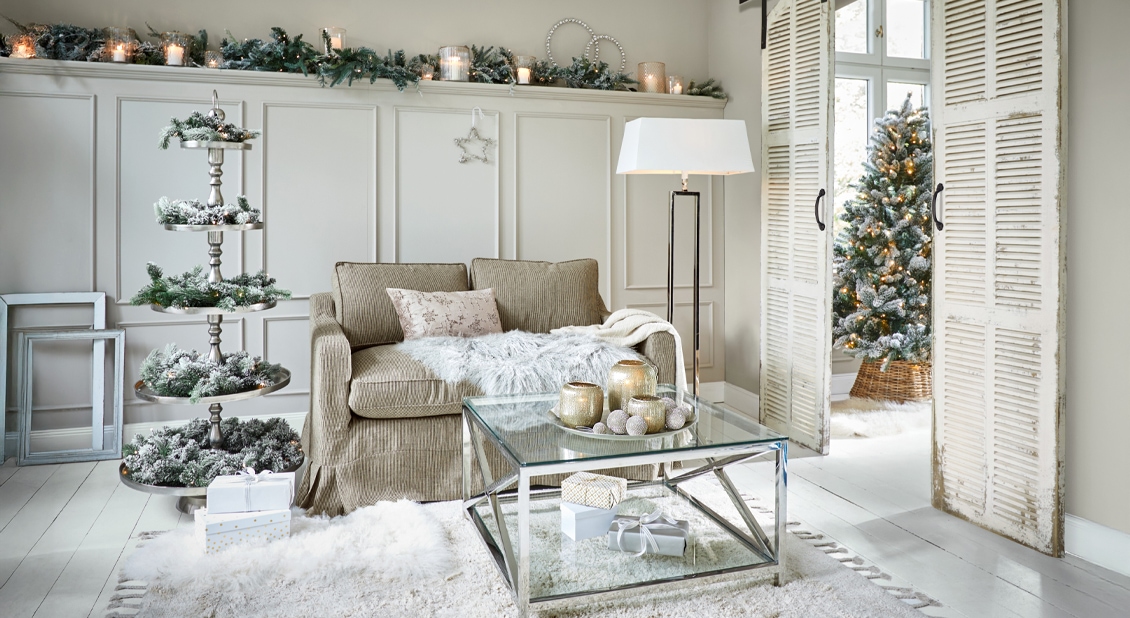 Salón acogedor con sofá beige, mesa de cristal y decoración navideña con árbol nevado y velas