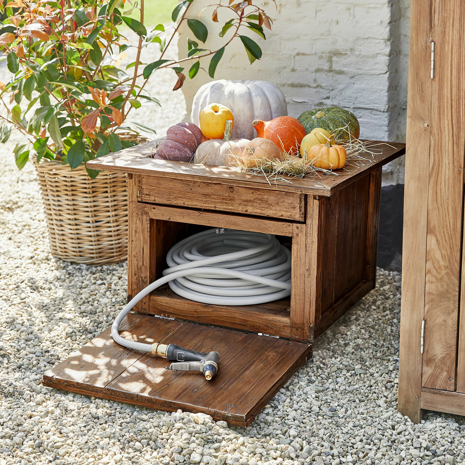 Caja de jardín de madera con manguera gris y calabazas decorativas encima