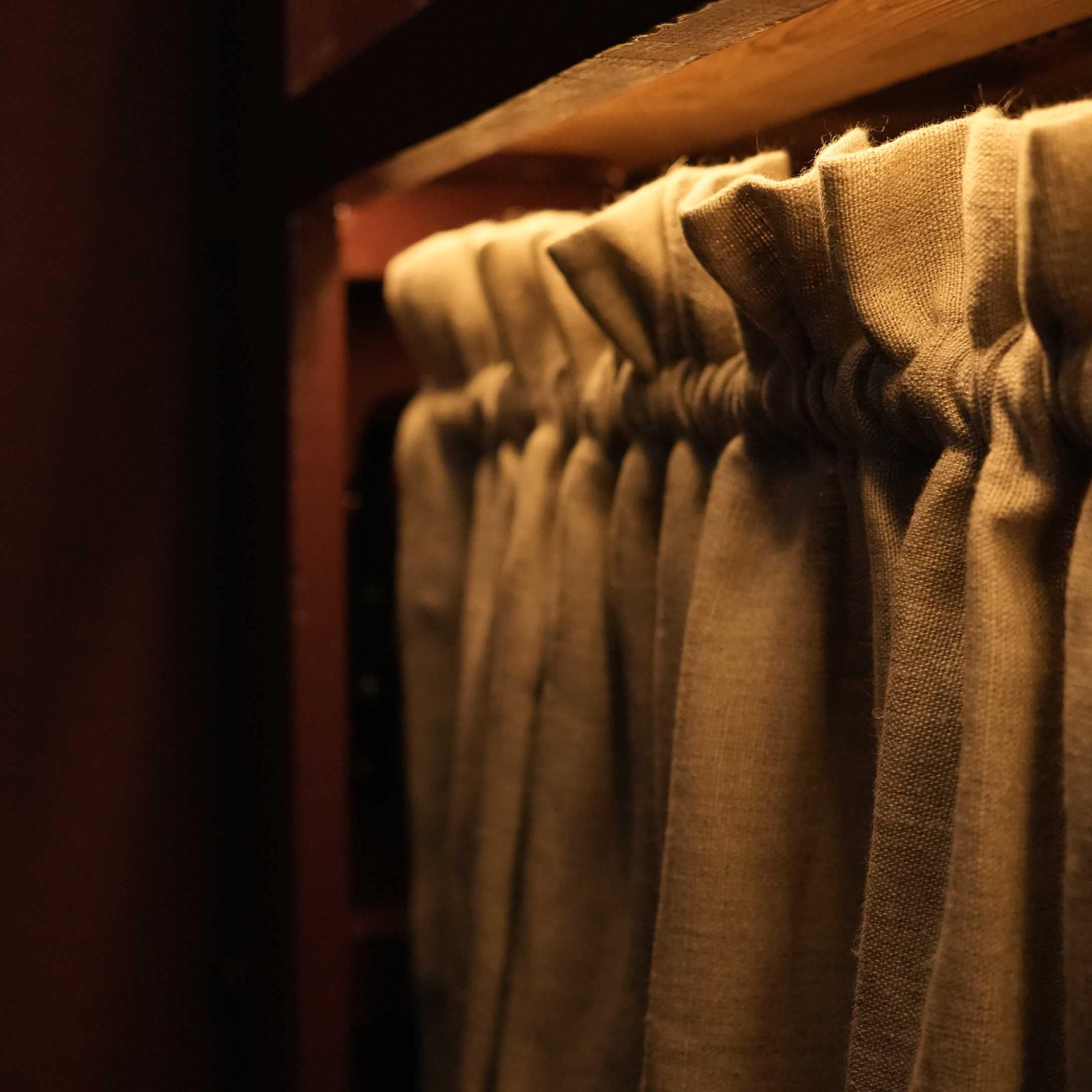 Cortina plisada de lino beige en barra de madera con luz cálida