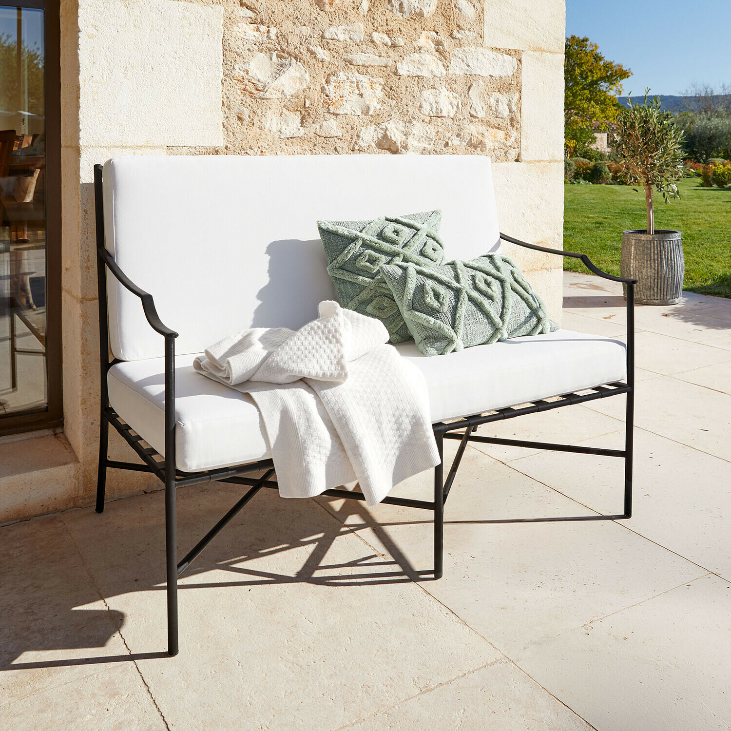 Sofá Vexford Banco de jardín de metal blanco con cojines suaves y cojines decorativos verdes en terraza soleada