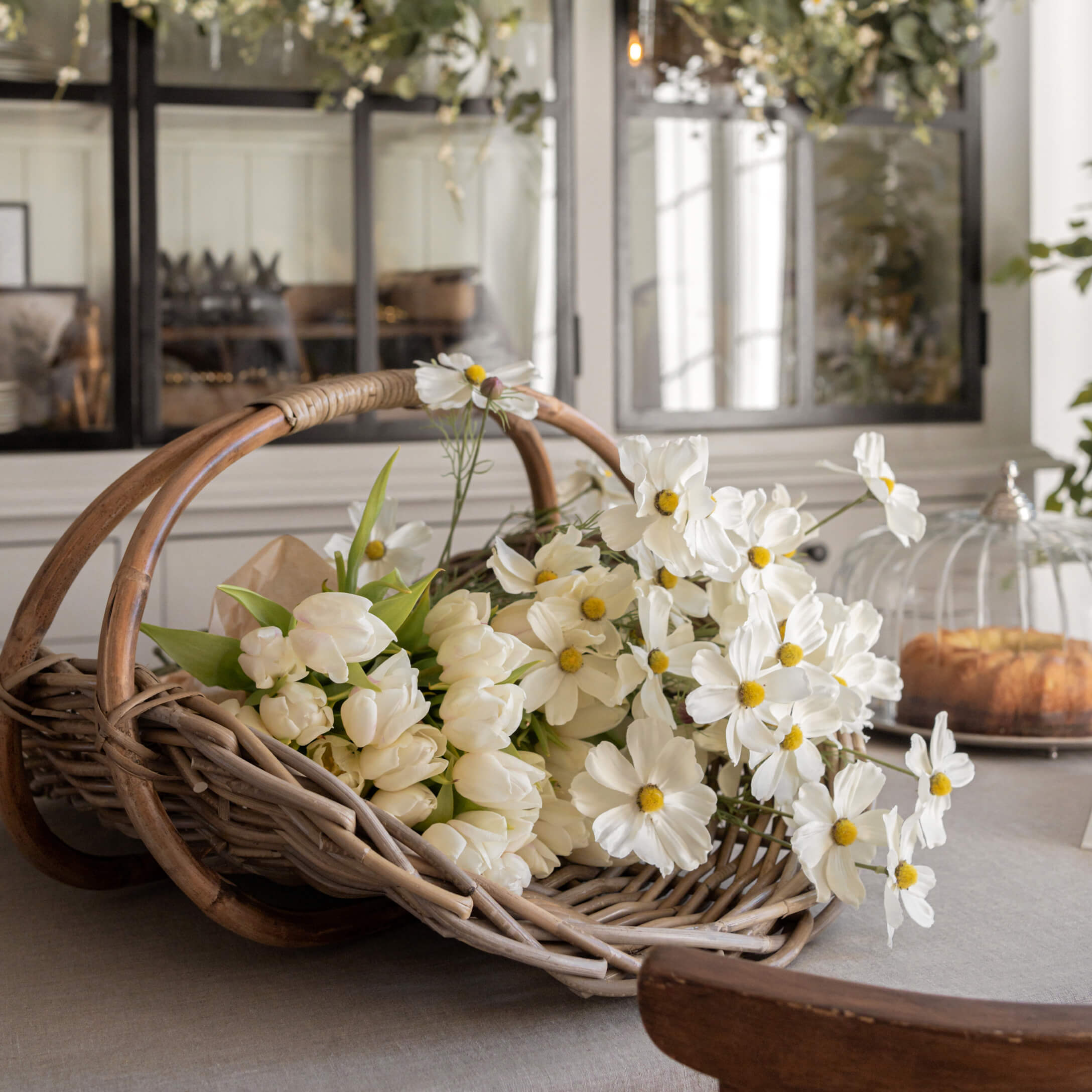 Cesta de mimbre con tulipanes blancos y flores decorativas sobre mesa en interior luminoso