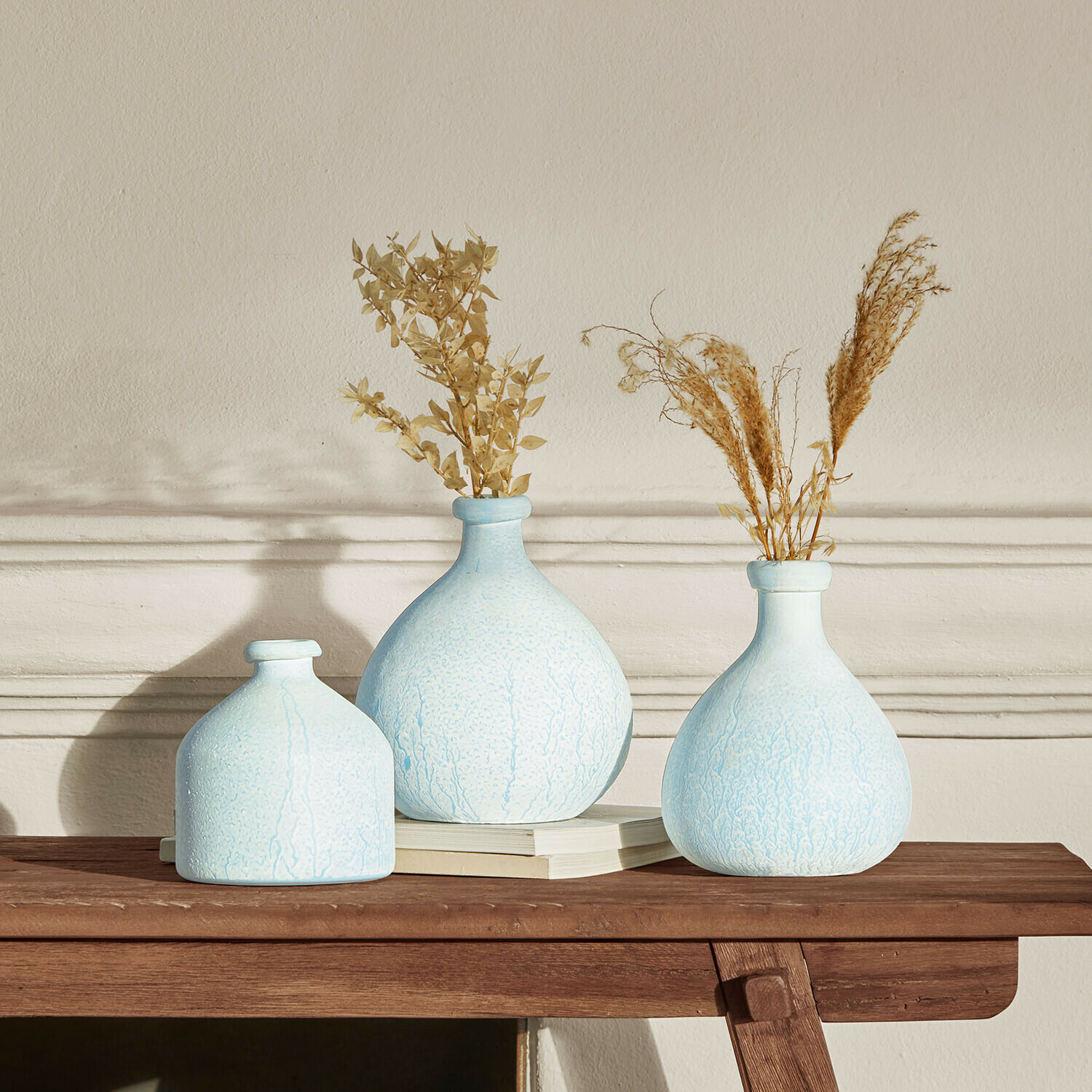 Conjunto de tres jarrones de cerámica azul claro con plantas secas sobre mesa de madera para decoración