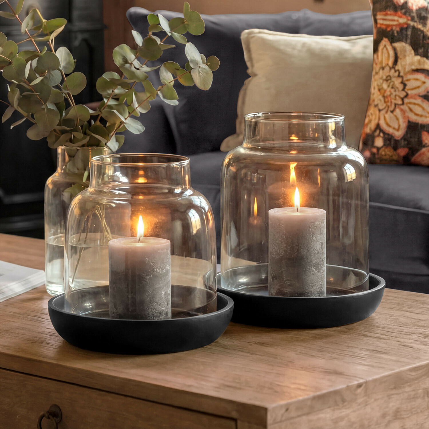 Set de 2 portavelas Venturio Velas grises en faroles de vidrio con bases negras sobre mesa de madera en sala de estar
