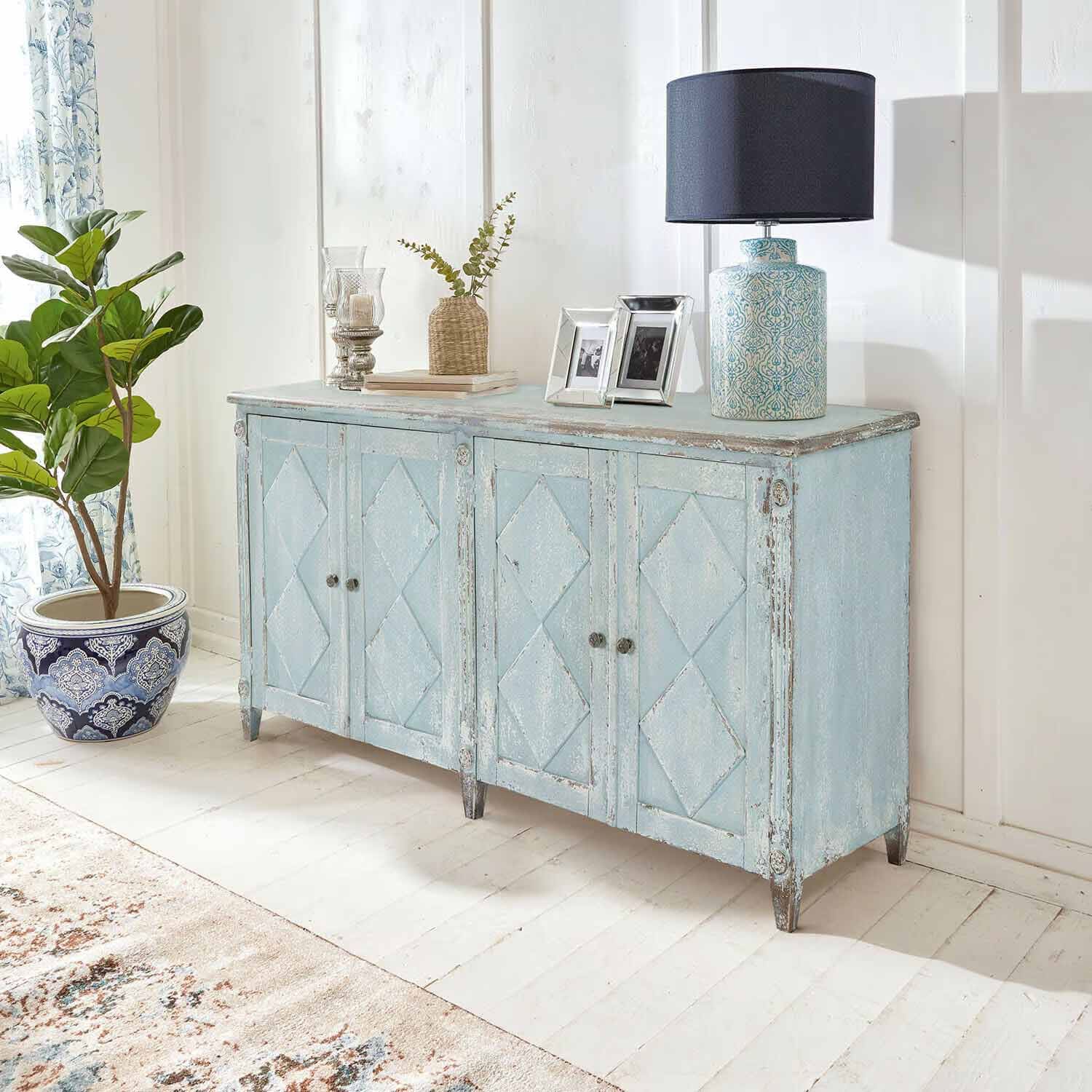 Aparador de madera azul envejecida estilo vintage en habitación luminosa con lámpara y planta decorativa