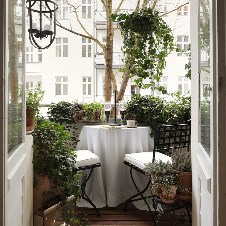 Balcón acogedor con mesa blanca, sillas negras y plantas verdes, ideal para relajarse.
