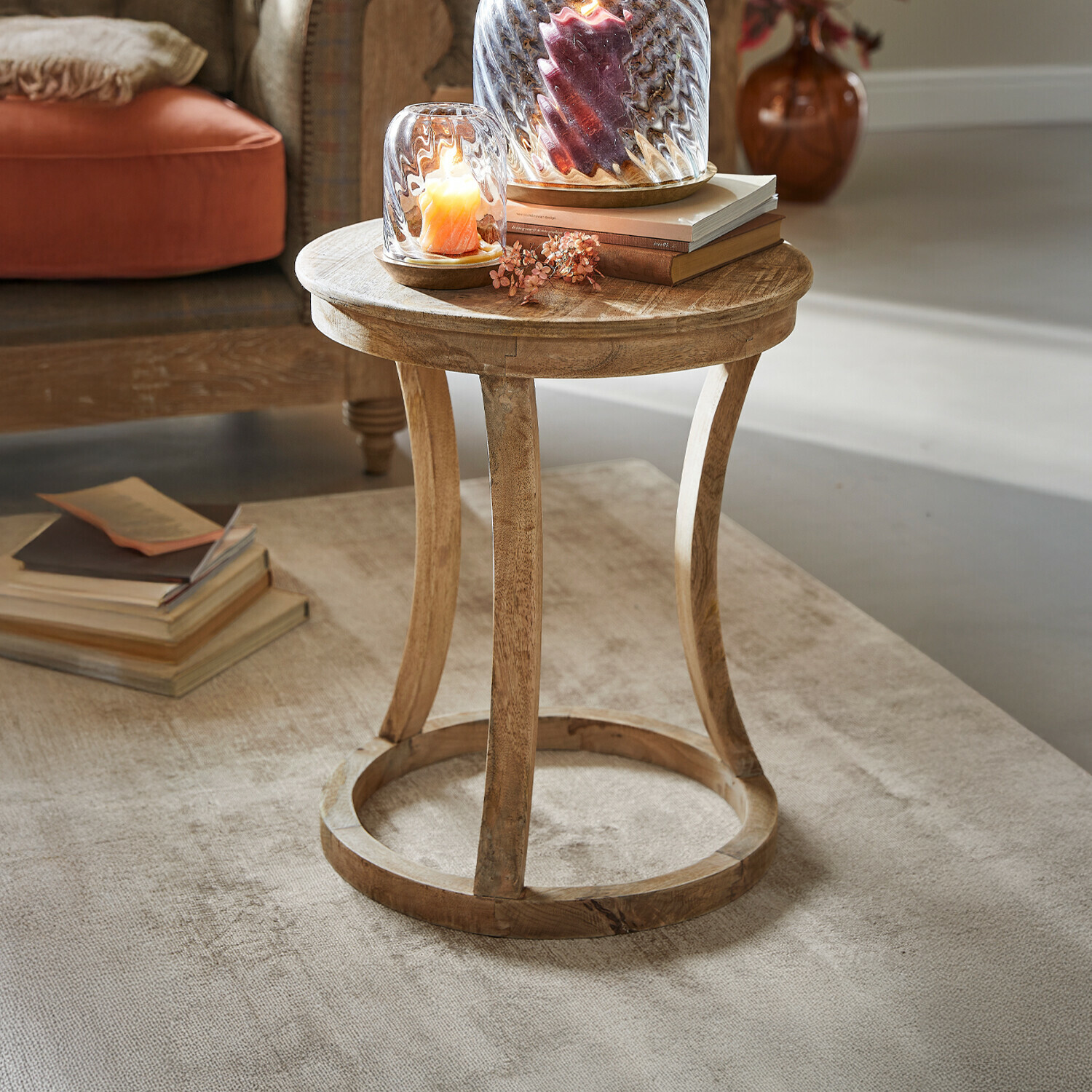 Mesa auxiliar East Harwich Mesa auxiliar redonda de madera de mango en color natural sobre alfombra clara con velas decorativas