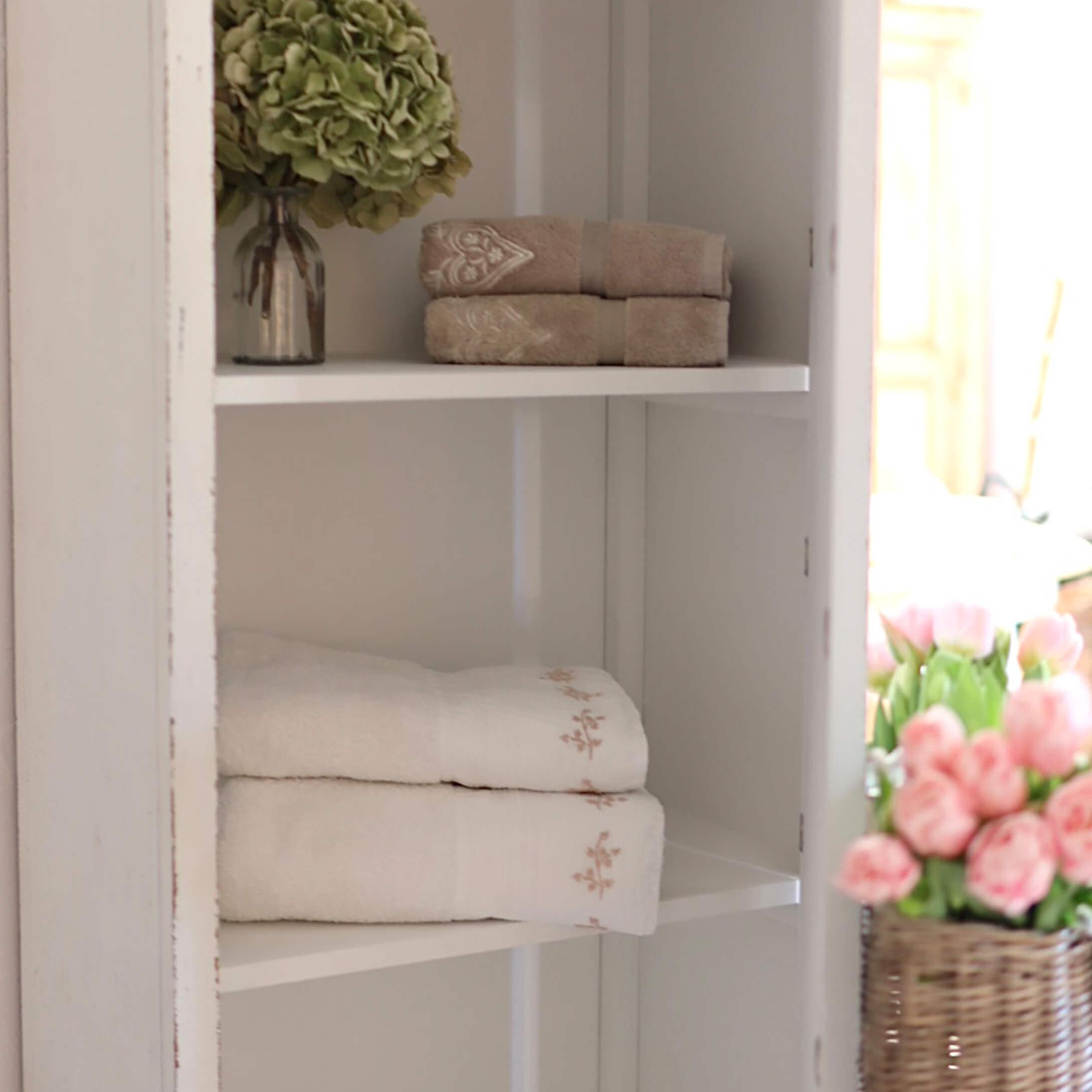 Toallas de algodón suaves en beige y blanco con bordado delicado en estante blanco