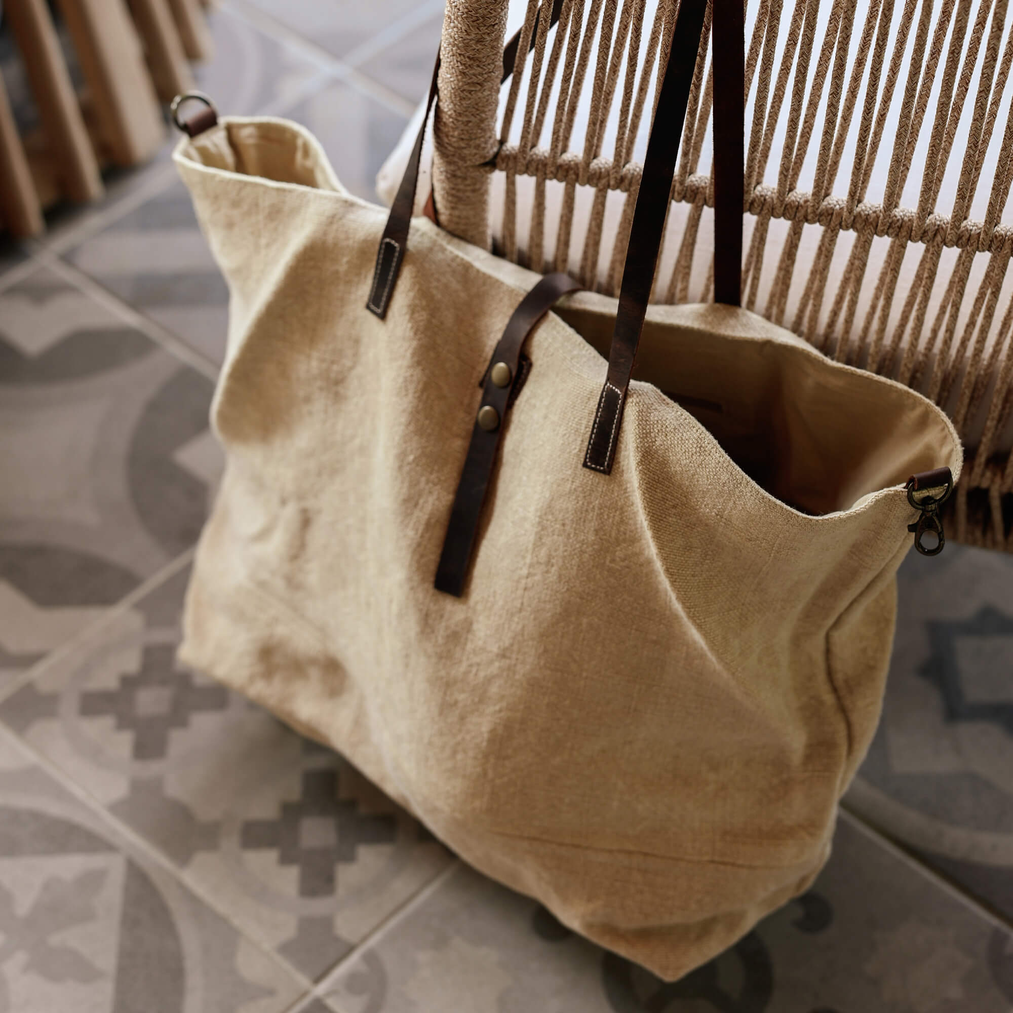 Bolsa beige de tela con asas de cuero marrón oscuro sobre suelo de baldosas con patrón