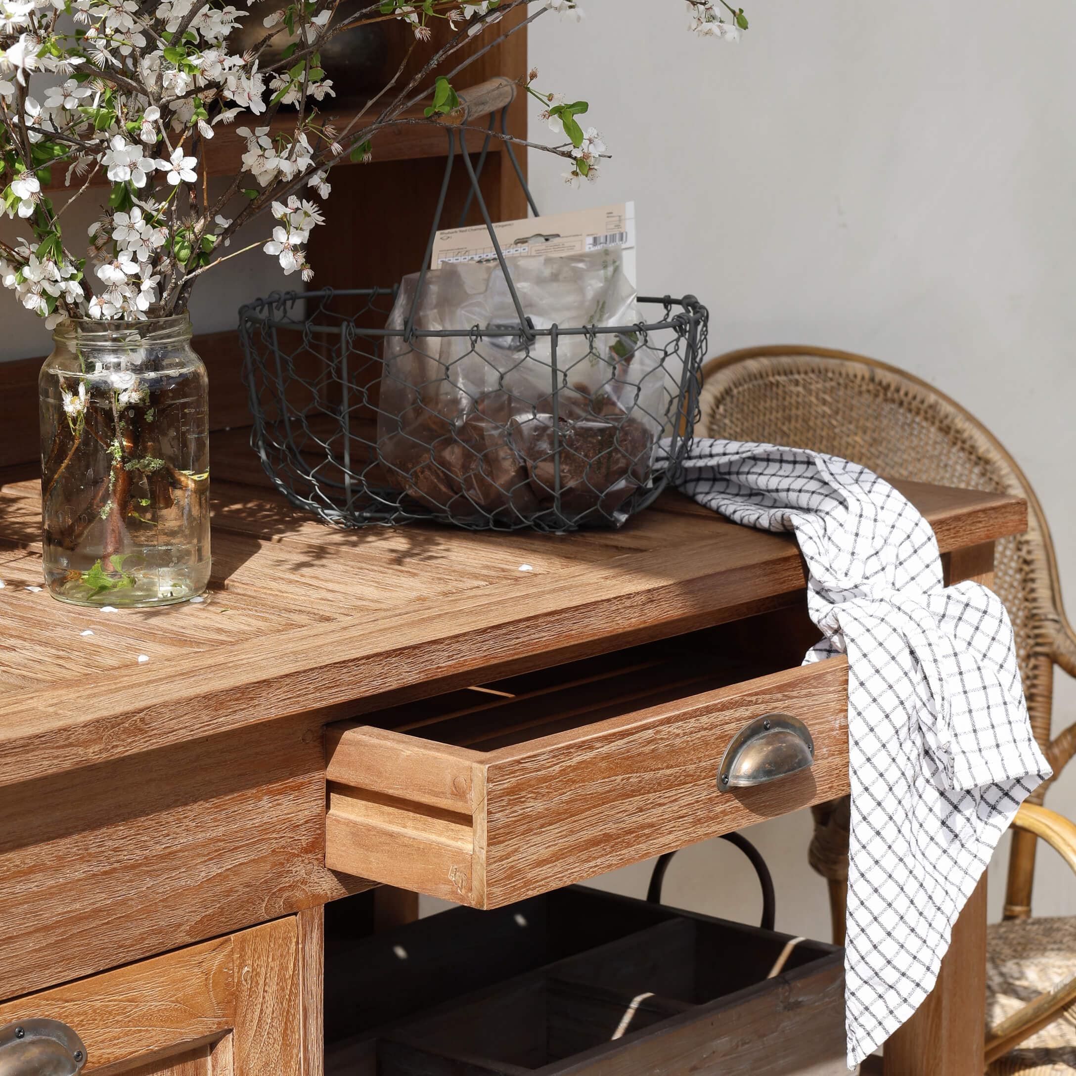 Mesa de madera con cajón abierto, cesta metálica y paño blanco a cuadros sobre la superficie