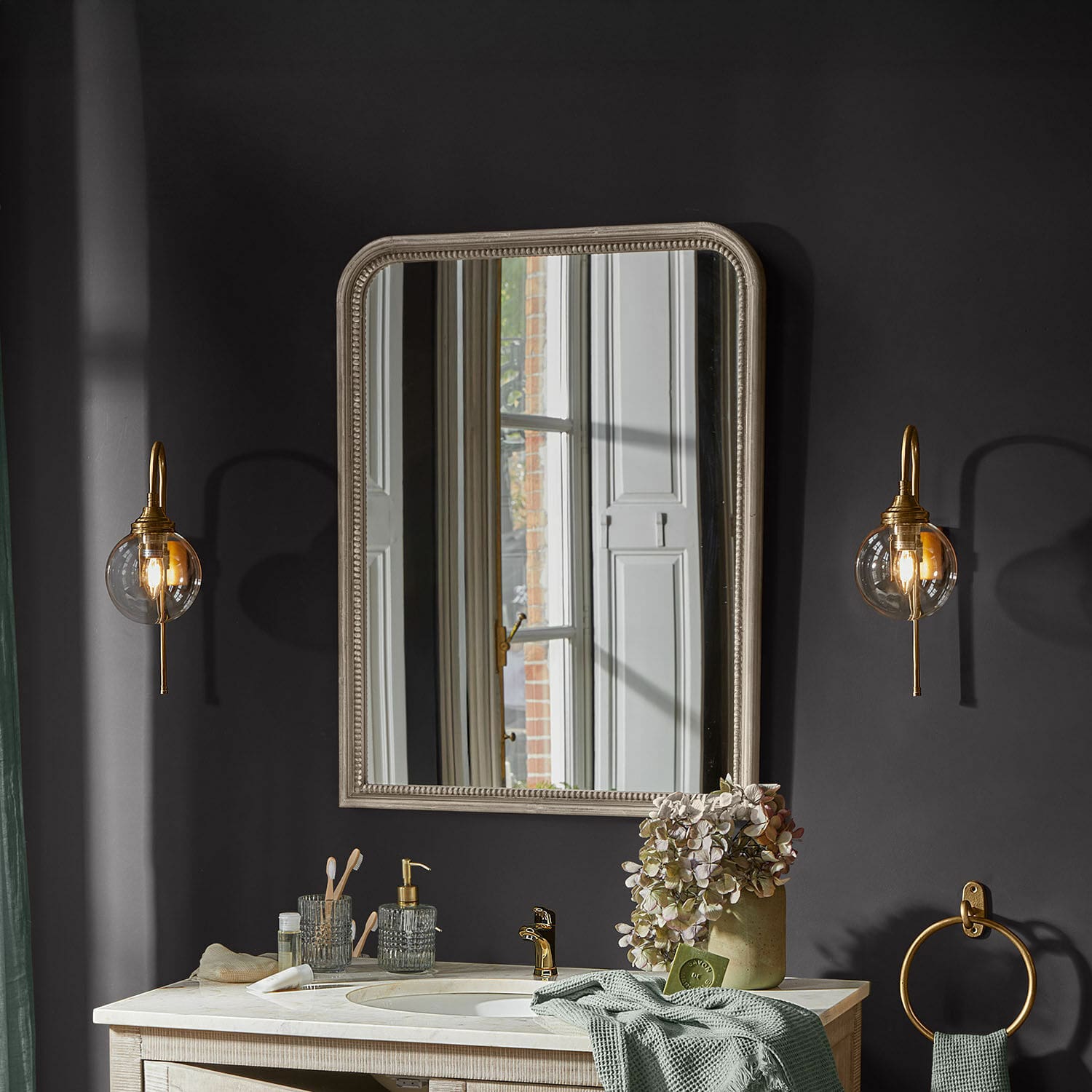 Espejo de baño beige con marco decorativo en pared oscura con apliques de latón
