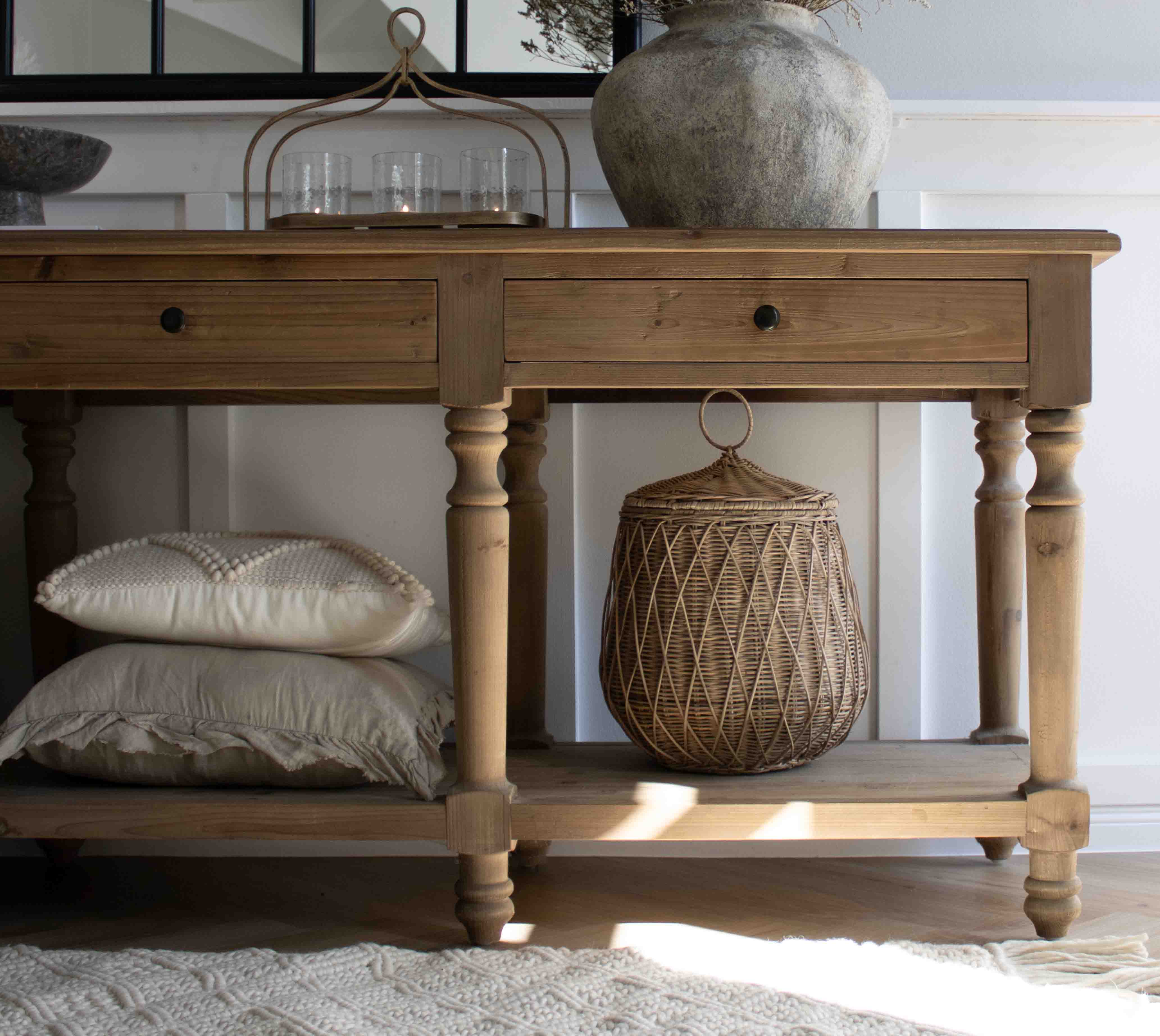 Mesa de madera natural con cajones, cesta de mimbre y cojines apilados debajo en ambiente acogedor