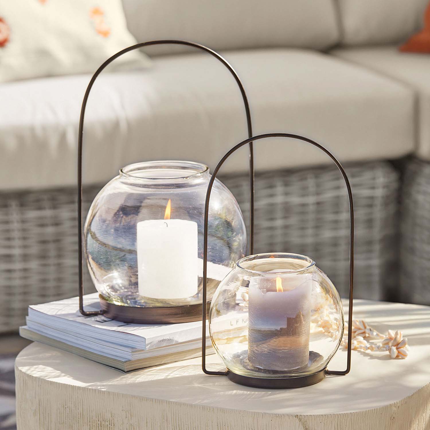 Faroles de vidrio con asas metálicas, velas blancas y grises, decoración de mesa en salón