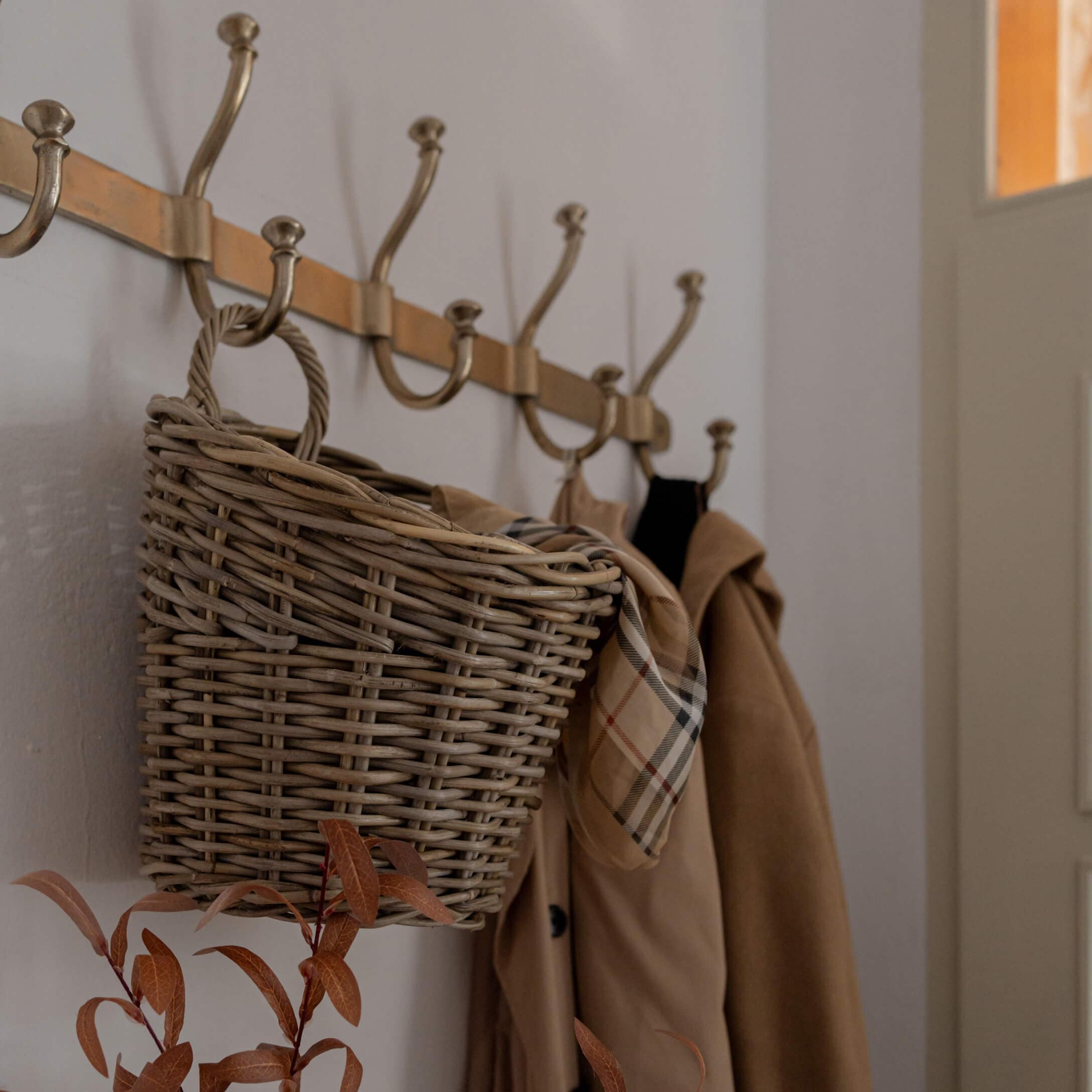 Cesta de mimbre colgada en perchero de latón con abrigo beige y bufanda a cuadros