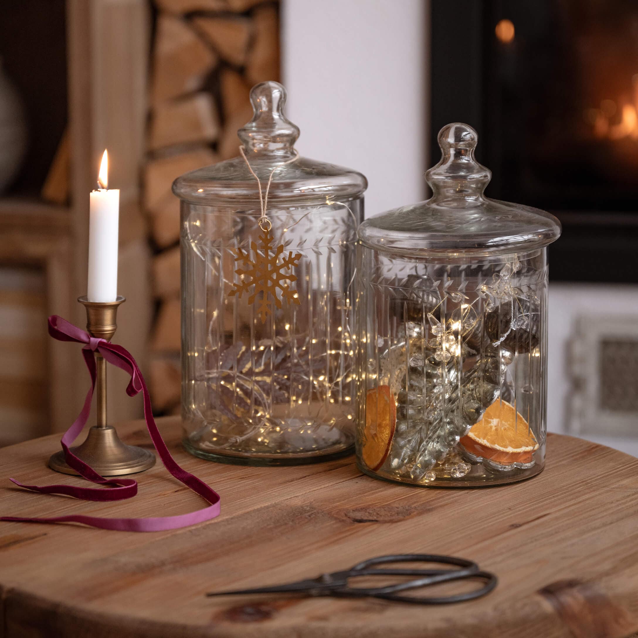 Tarros de vidrio transparentes con tapas sobre mesa de madera, decorados con luces y vela encendida
