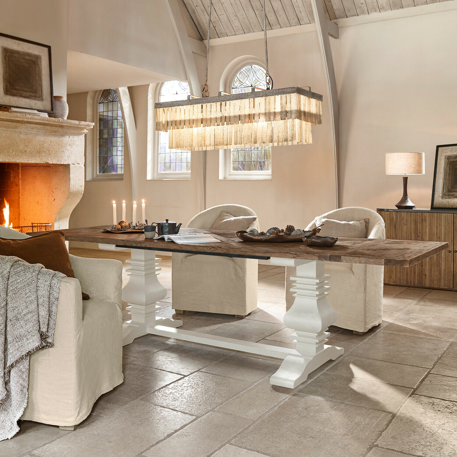 Mesa grande de madera con base blanca en salón luminoso con chimenea y sillones beige