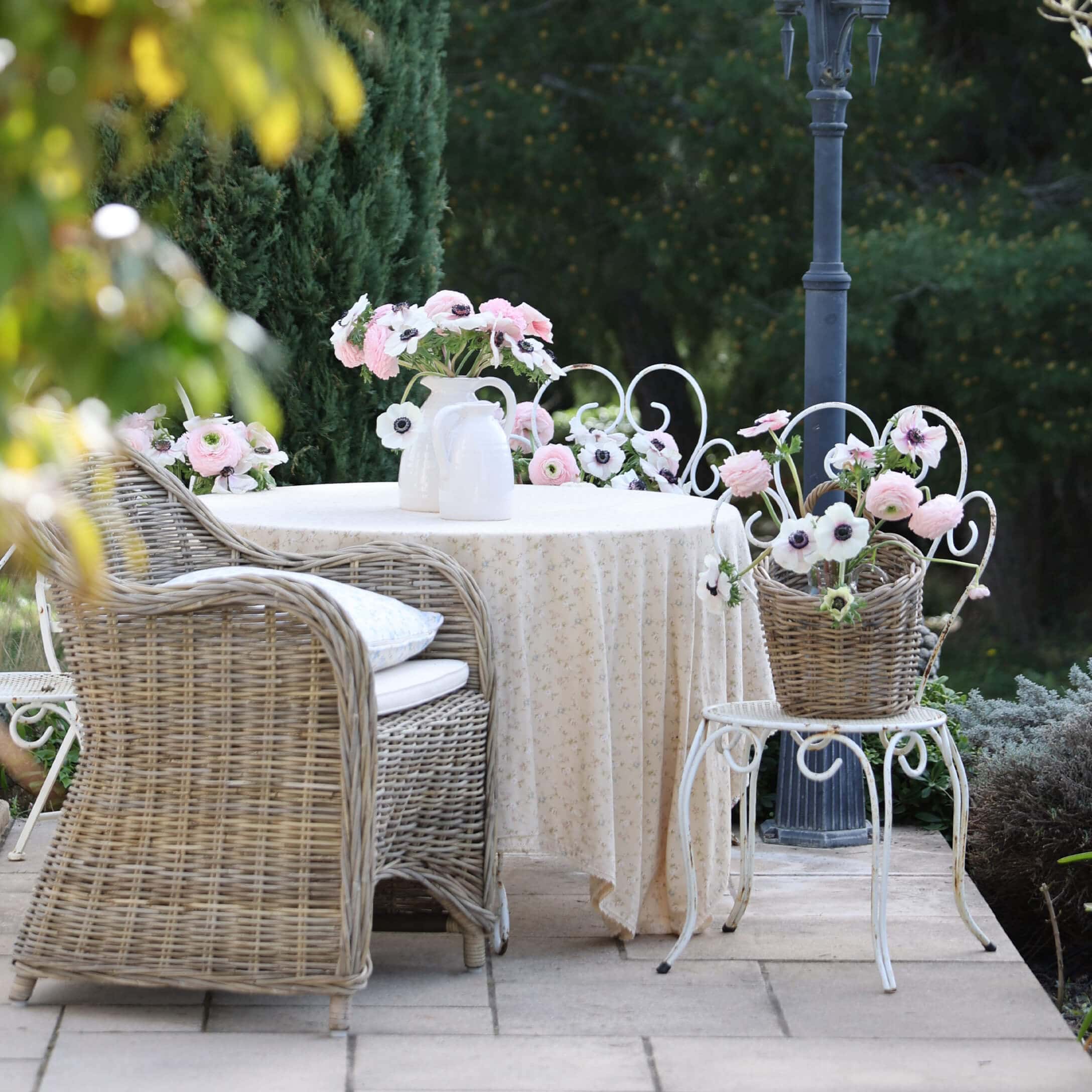 Jardín con sillón de mimbre, mesa blanca con mantel y flores en jarrones, ambiente romántico
