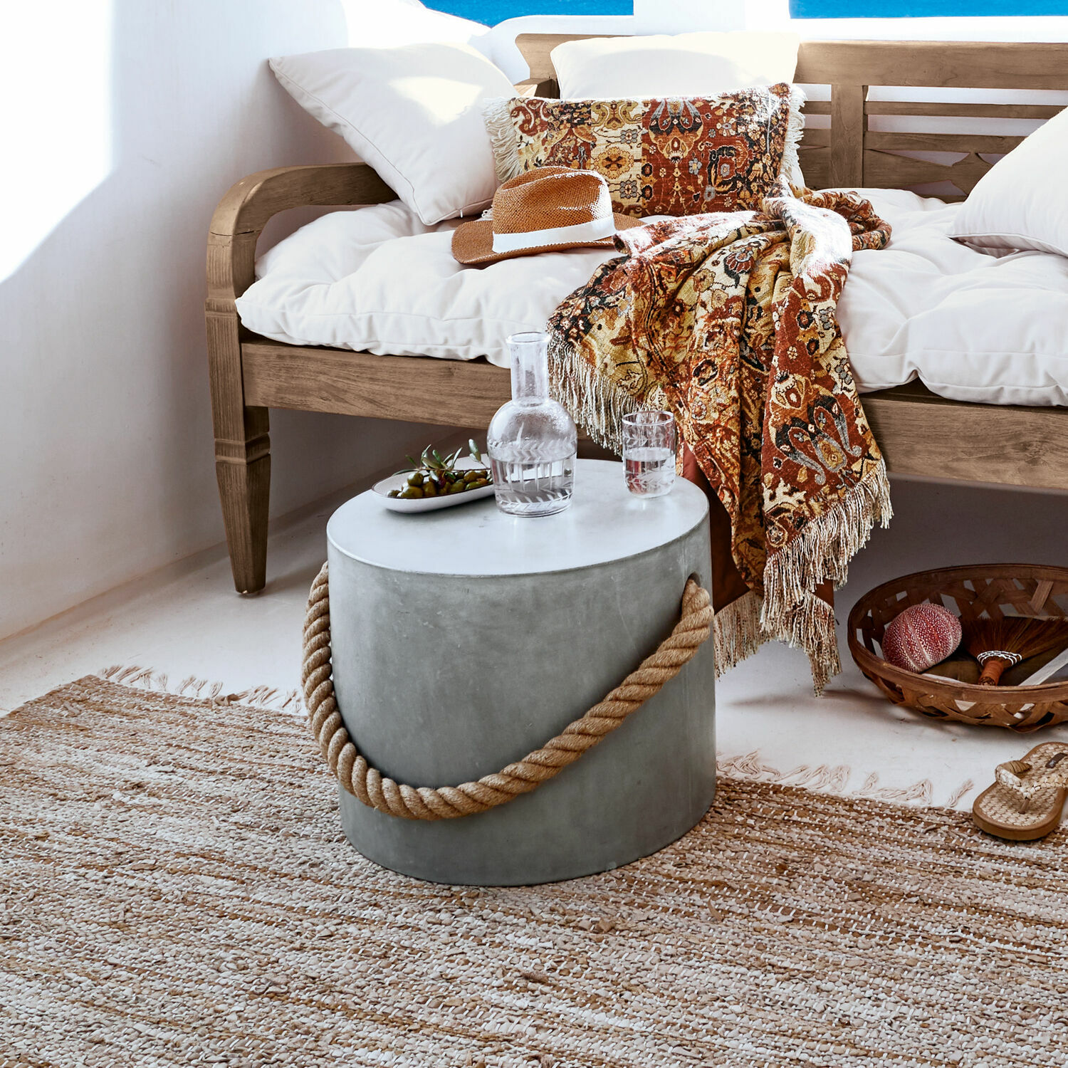 Puf Kaedi Mesa redonda de hormigón con asa de cuerda en salón natural con sofá de madera y manta decorativa