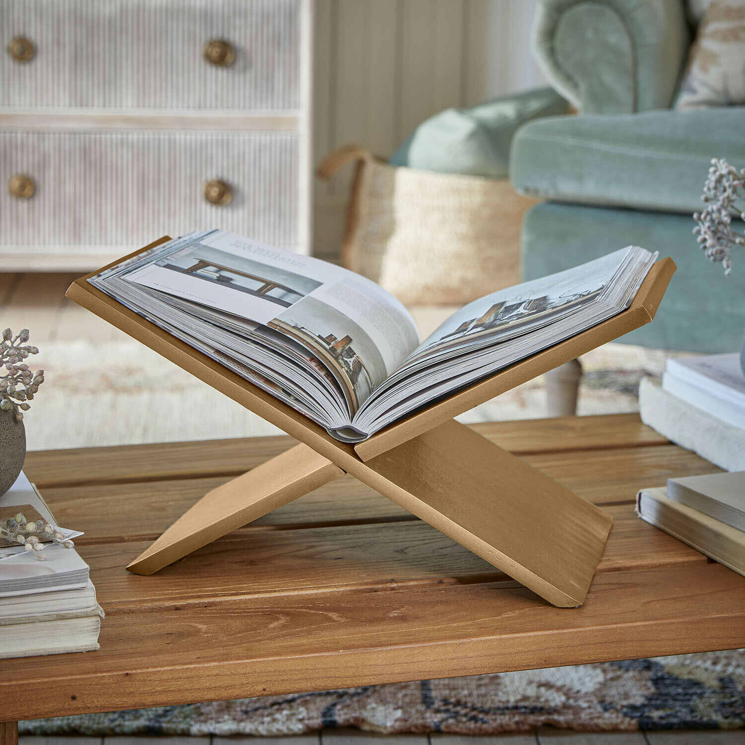 Revistero Rashira Soporte dorado de madera para libros sobre mesa de centro en salón acogedor con sofá verde