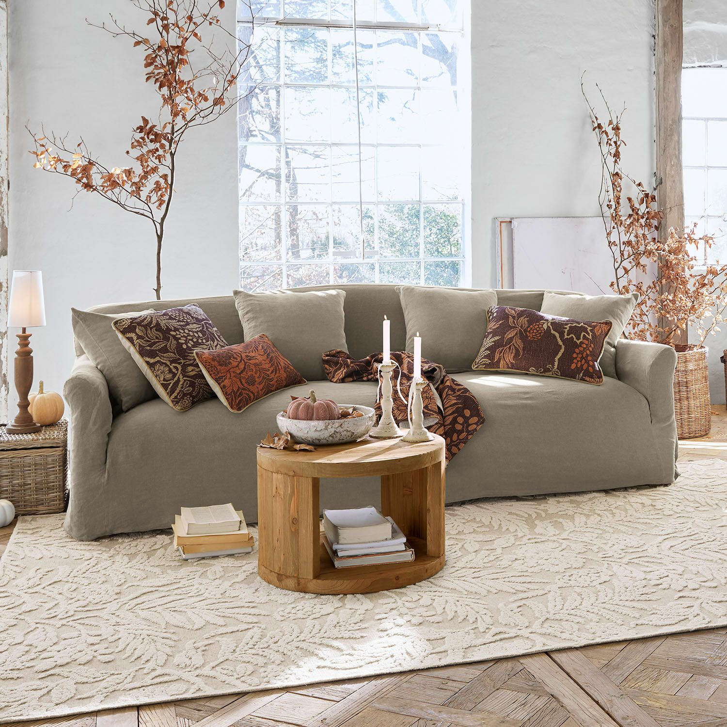 Sofá Riveneuve Sofá beige de tela en sala luminosa con mesa de madera redonda y decoración otoñal