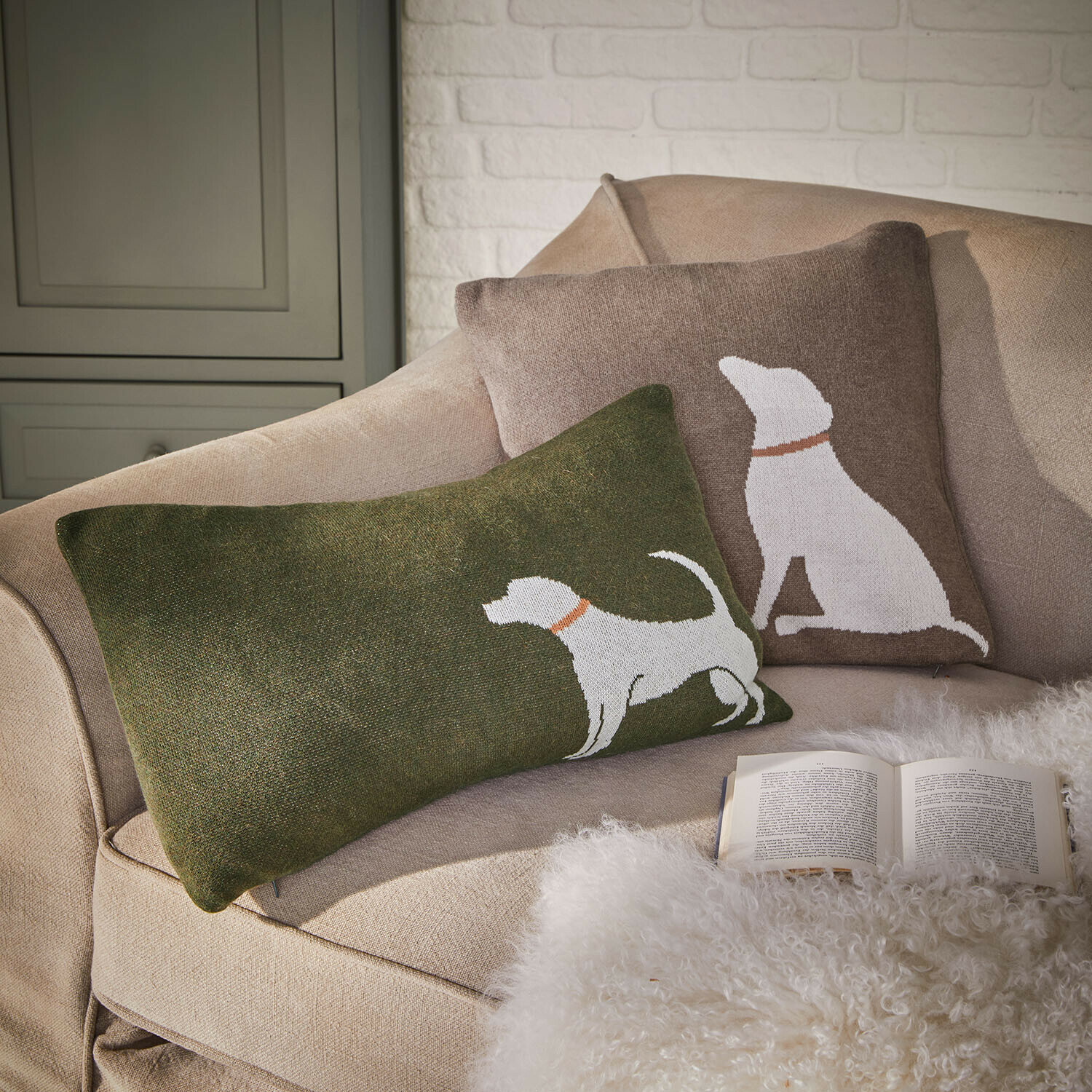 Set de 2 fundas de cojín Olyden Conjunto de dos cojines decorativos con diseño de perro blanco sobre fondo verde y marrón en sofá beige