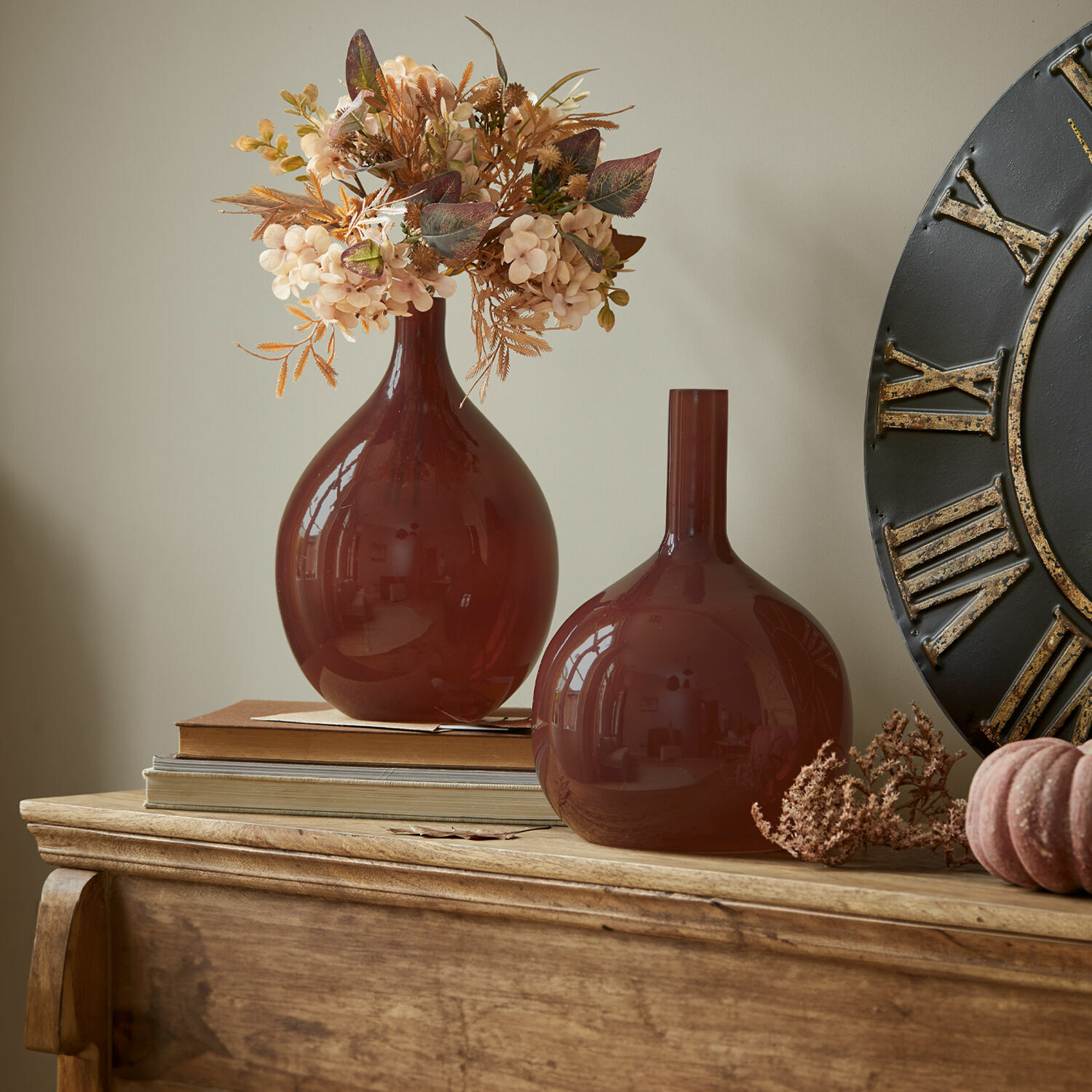 Dos jarrones de vidrio marrón sobre mesa de madera con flores secas decorativas y libros