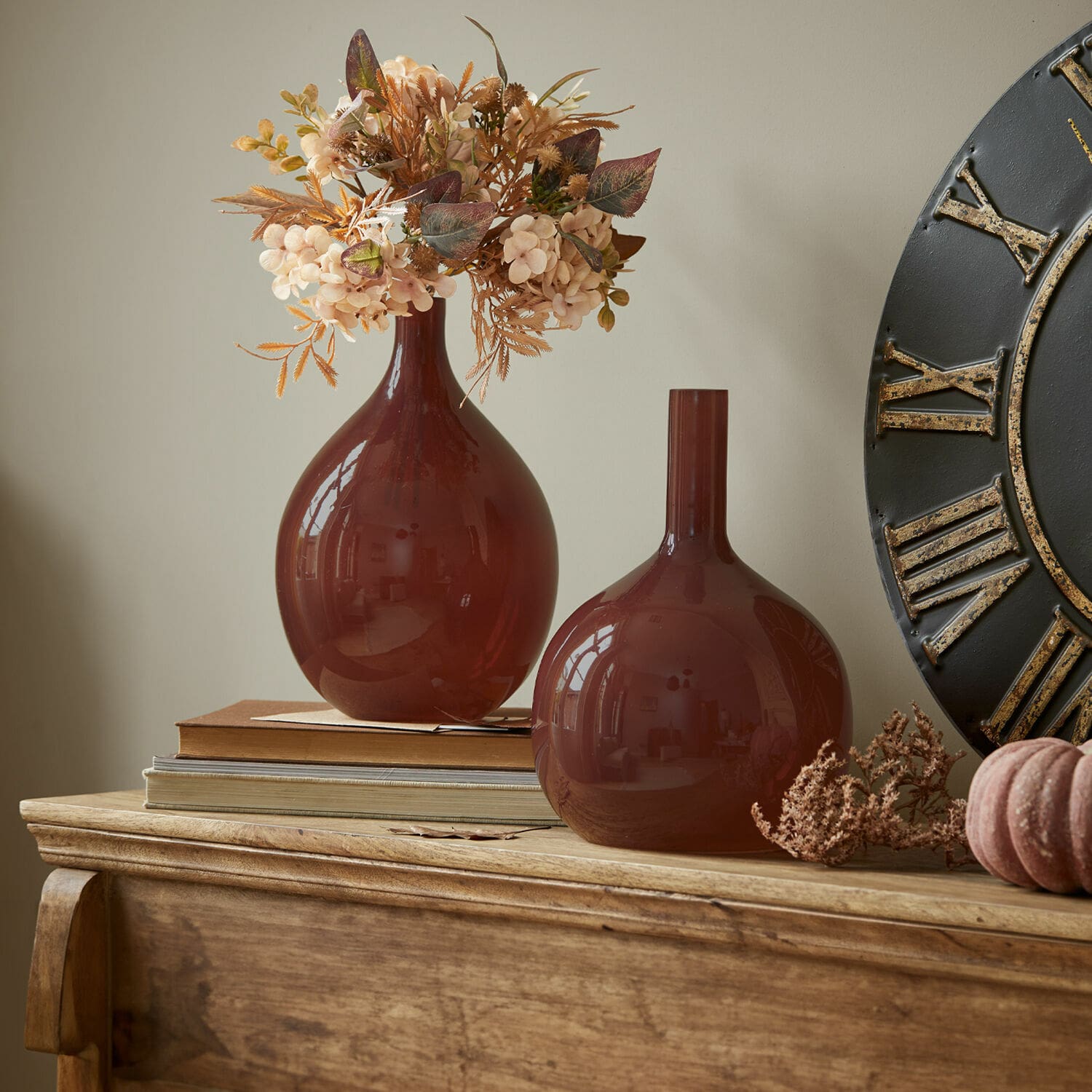 Set de 2 jarrones Erlunda Dos jarrones de vidrio marrón sobre mesa de madera con flores secas decorativas y libros