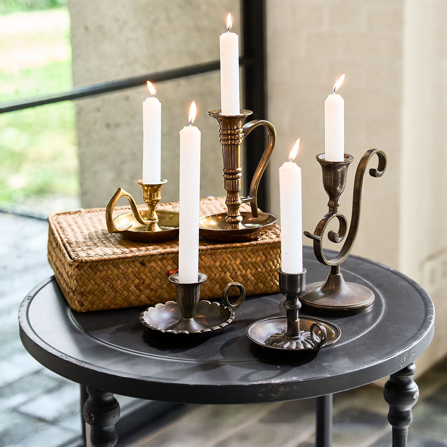 Conjunto de candelabros metálicos con velas blancas sobre mesa redonda negra para decoración interior
