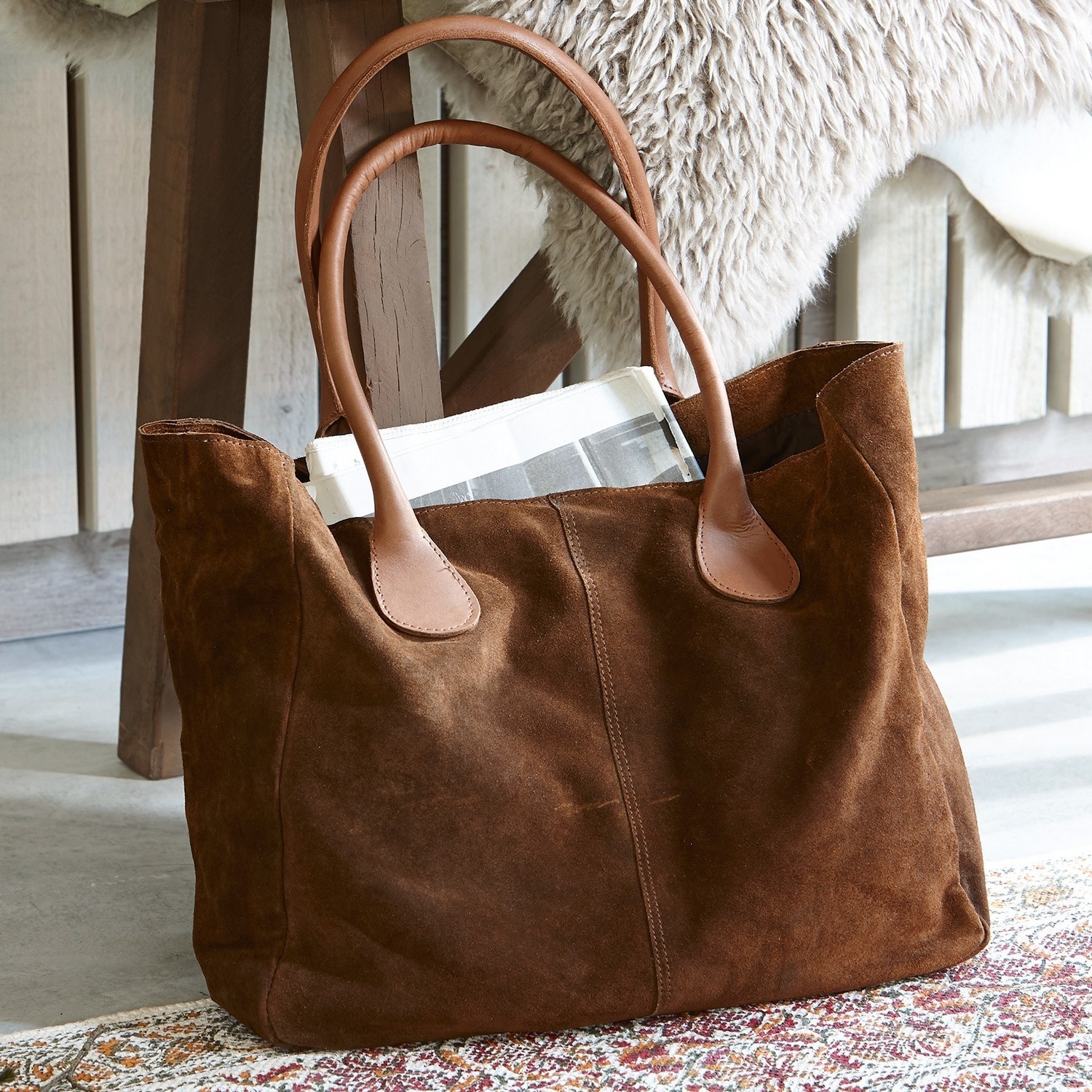 Bolso Genevielle Bolso de ante marrón con asas de cuero claro sobre alfombra junto a silla de madera