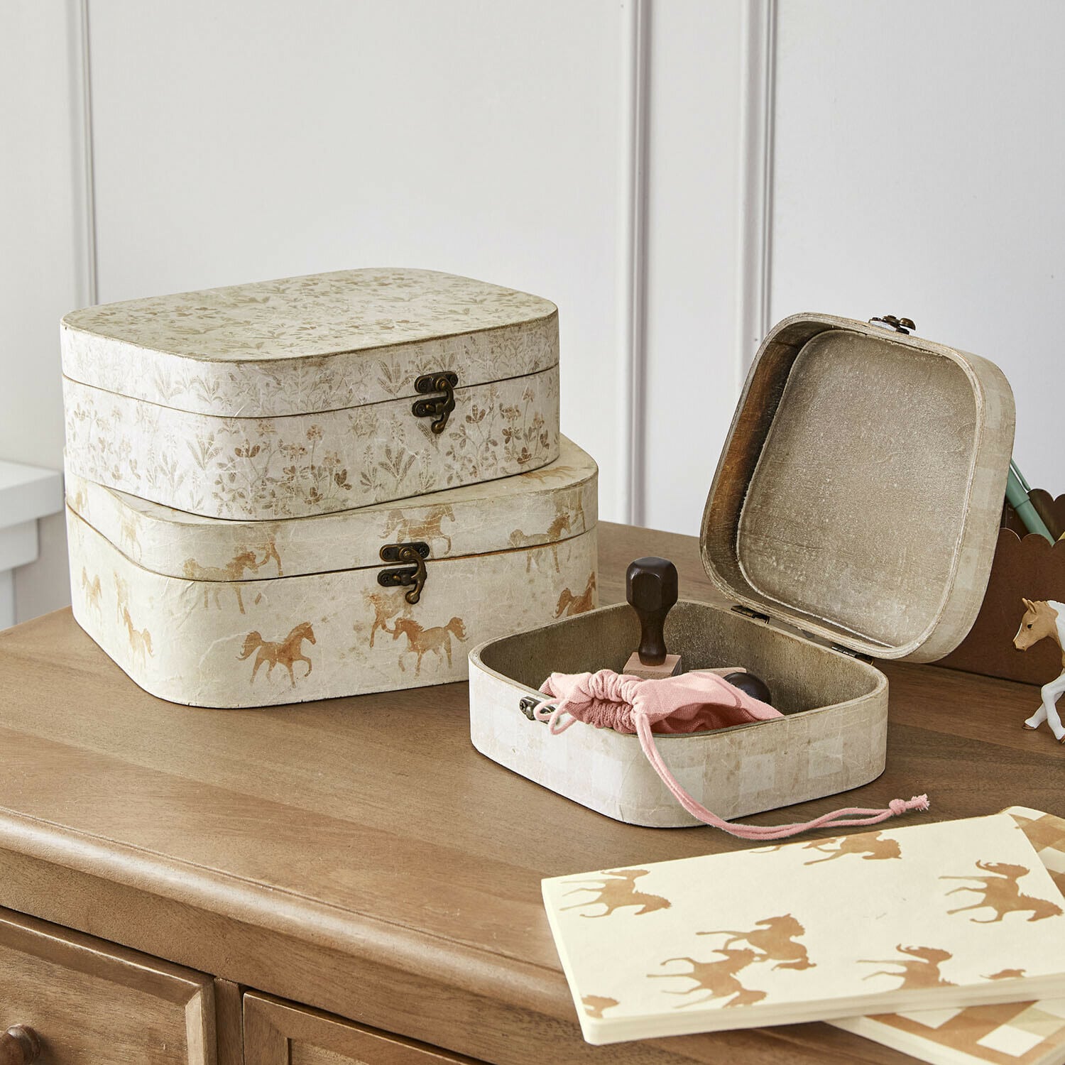Conjunto de tres cajas decorativas de papel beige con motivos de caballos y flores sobre mesa de madera