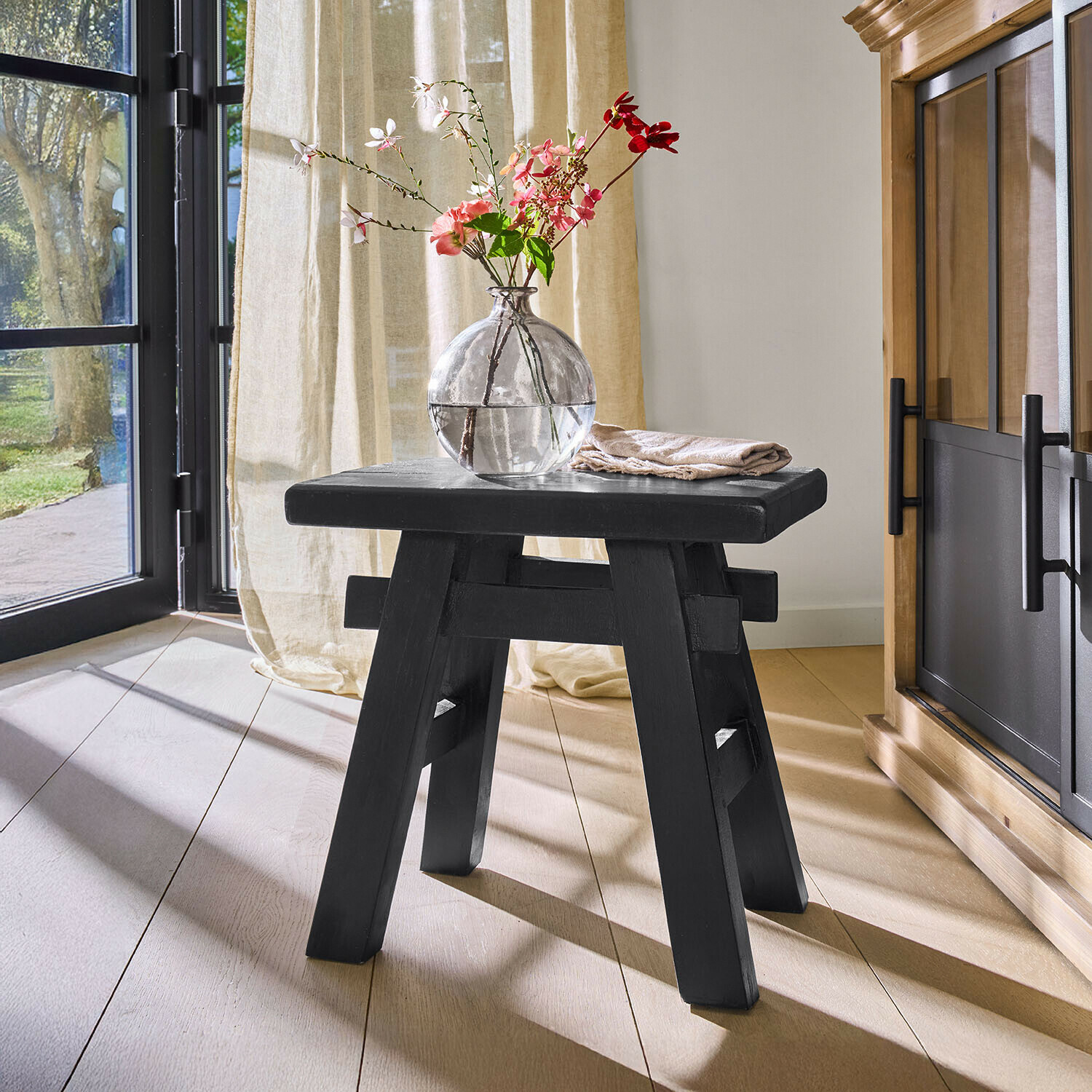 Taburete Oaklynne Taburete de madera negro con diseño sencillo en habitación luminosa con jarrón y flores