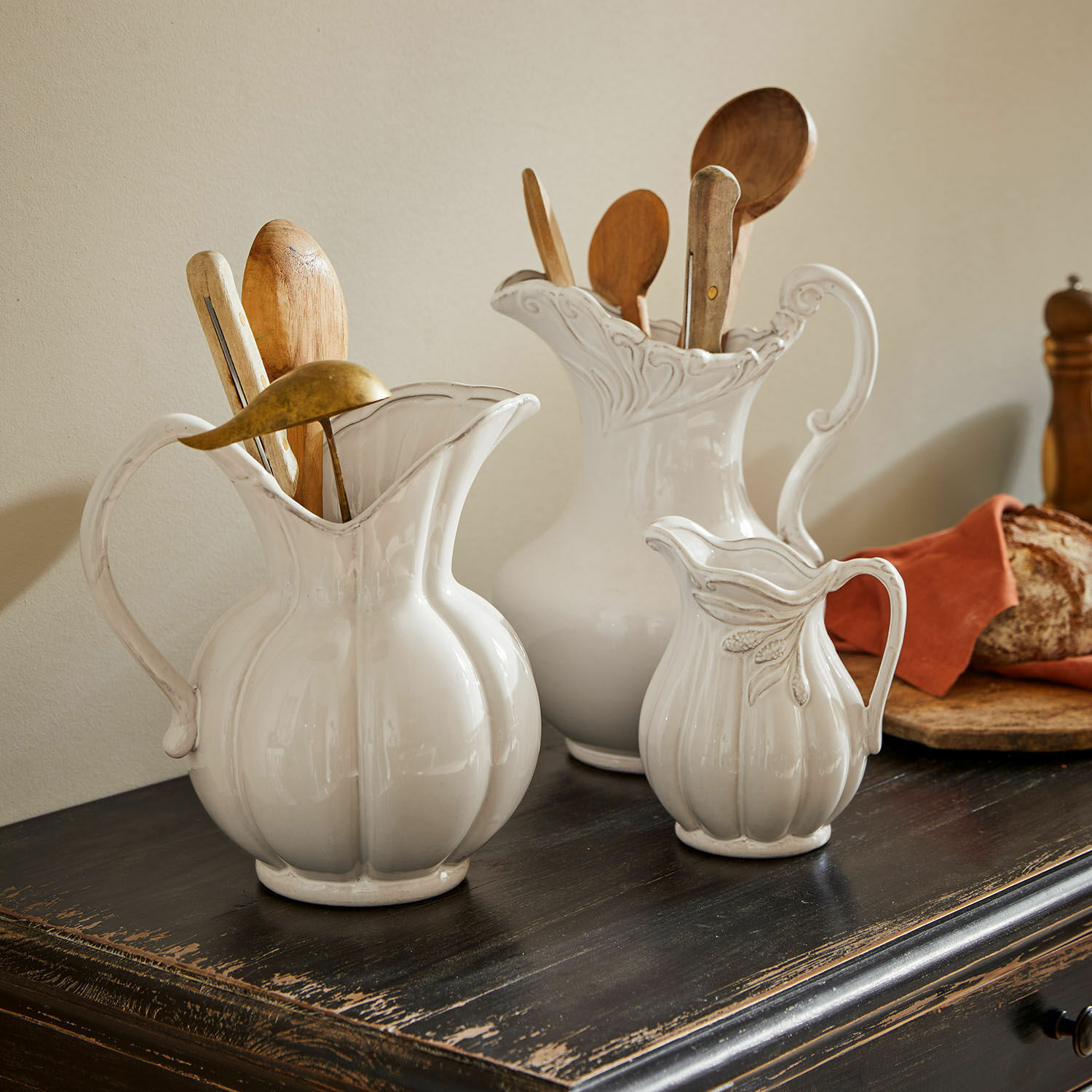 Set de 3 jarras Lucanera Tres jarras de cerámica blanca sobre mesa de madera oscura con cucharas de madera y pan