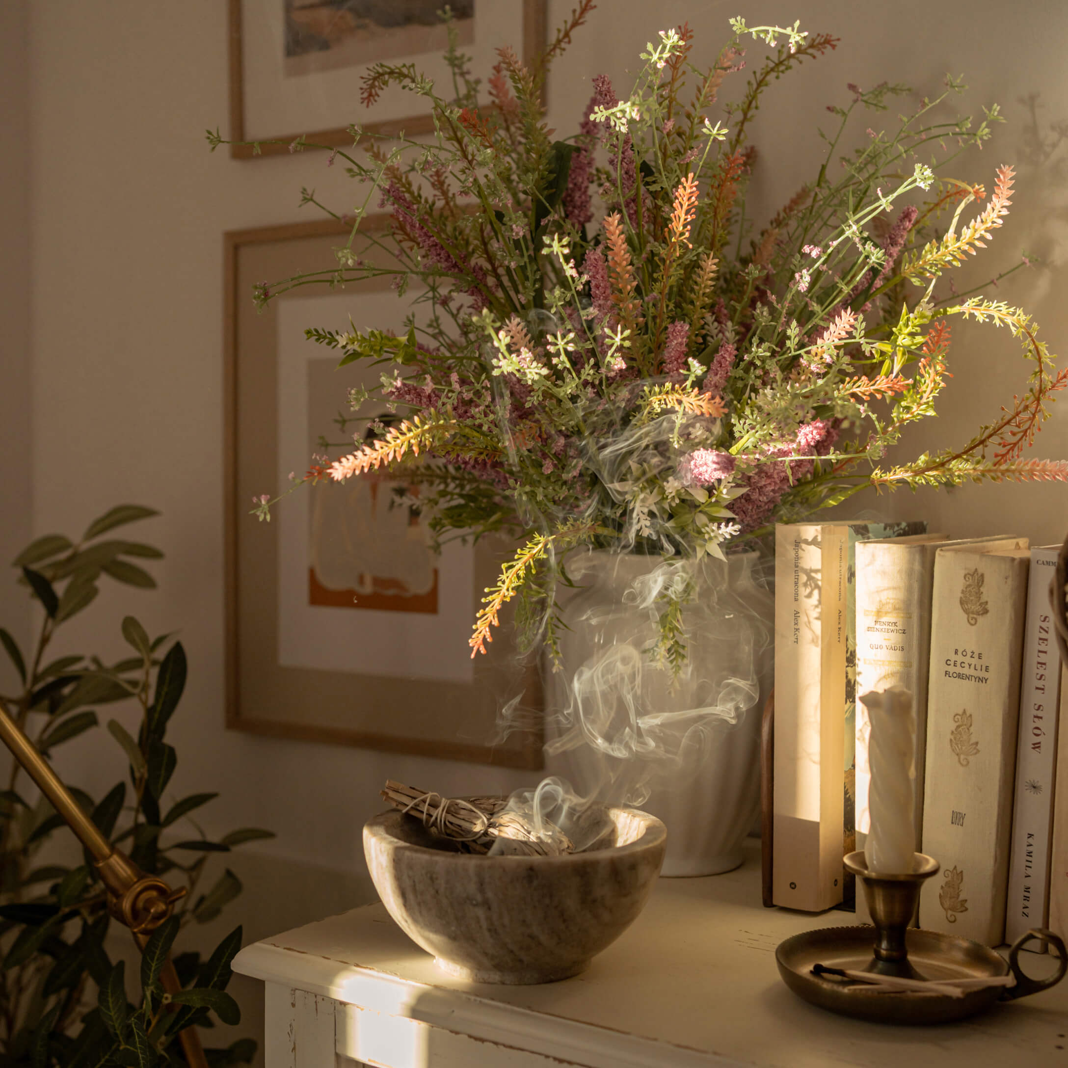 Cuenco de alabastro con salvia humeante junto a jarrón con flores coloridas y libros sobre mesa