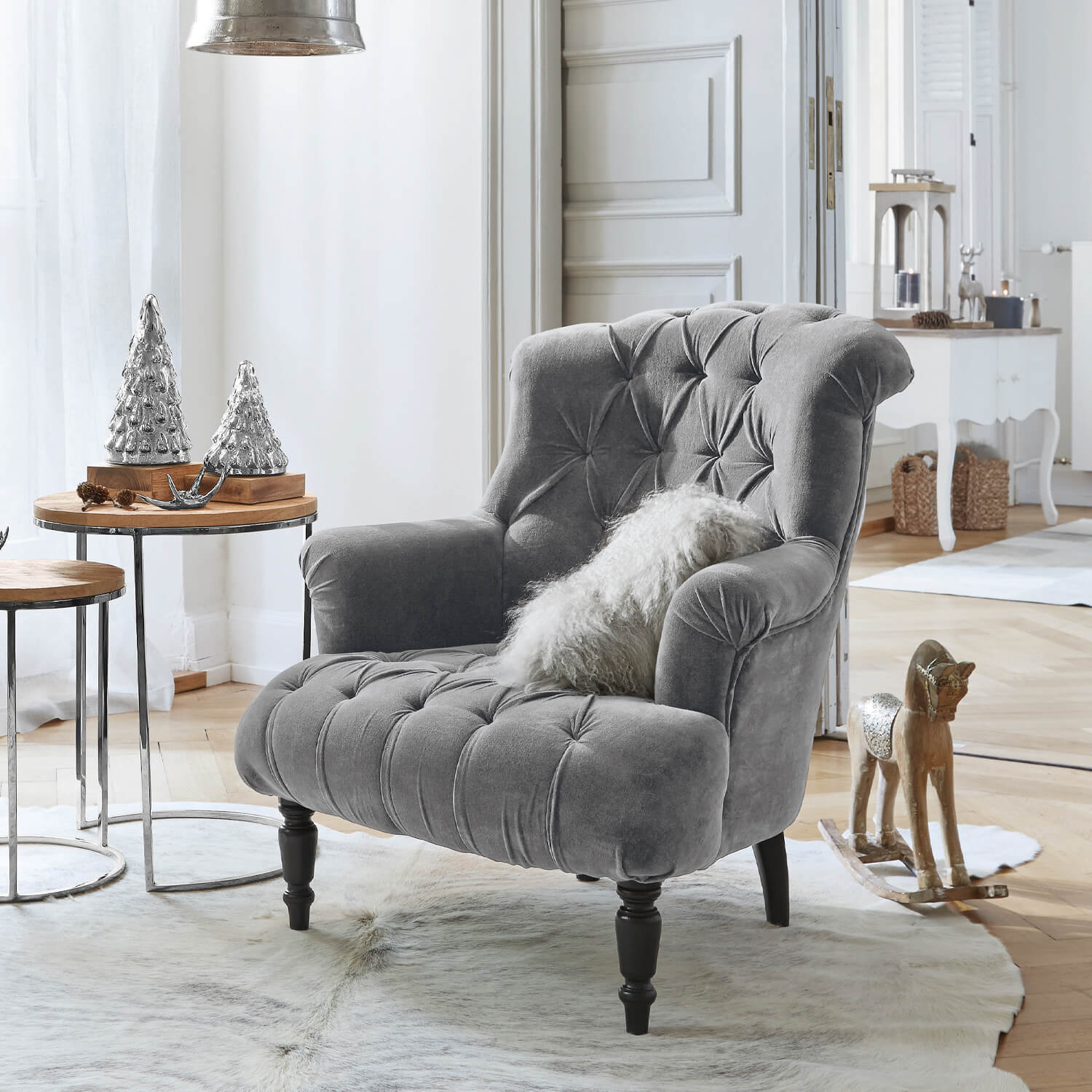 Sillón gris de terciopelo con respaldo capitoné y patas negras en salón luminoso con decoración navideña