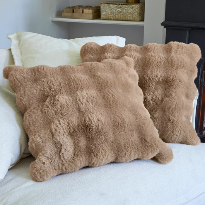 Cojines beige suaves de material peludo sobre sofá claro, decoración interior acogedora