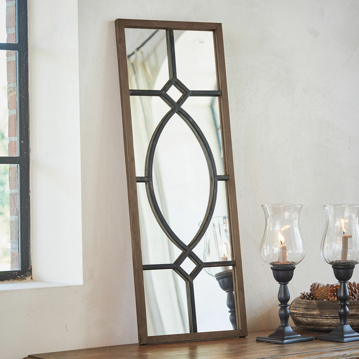 Espejo Millery Espejo rectangular con marco de madera marrón y diseño metálico negro sobre mesa con faroles