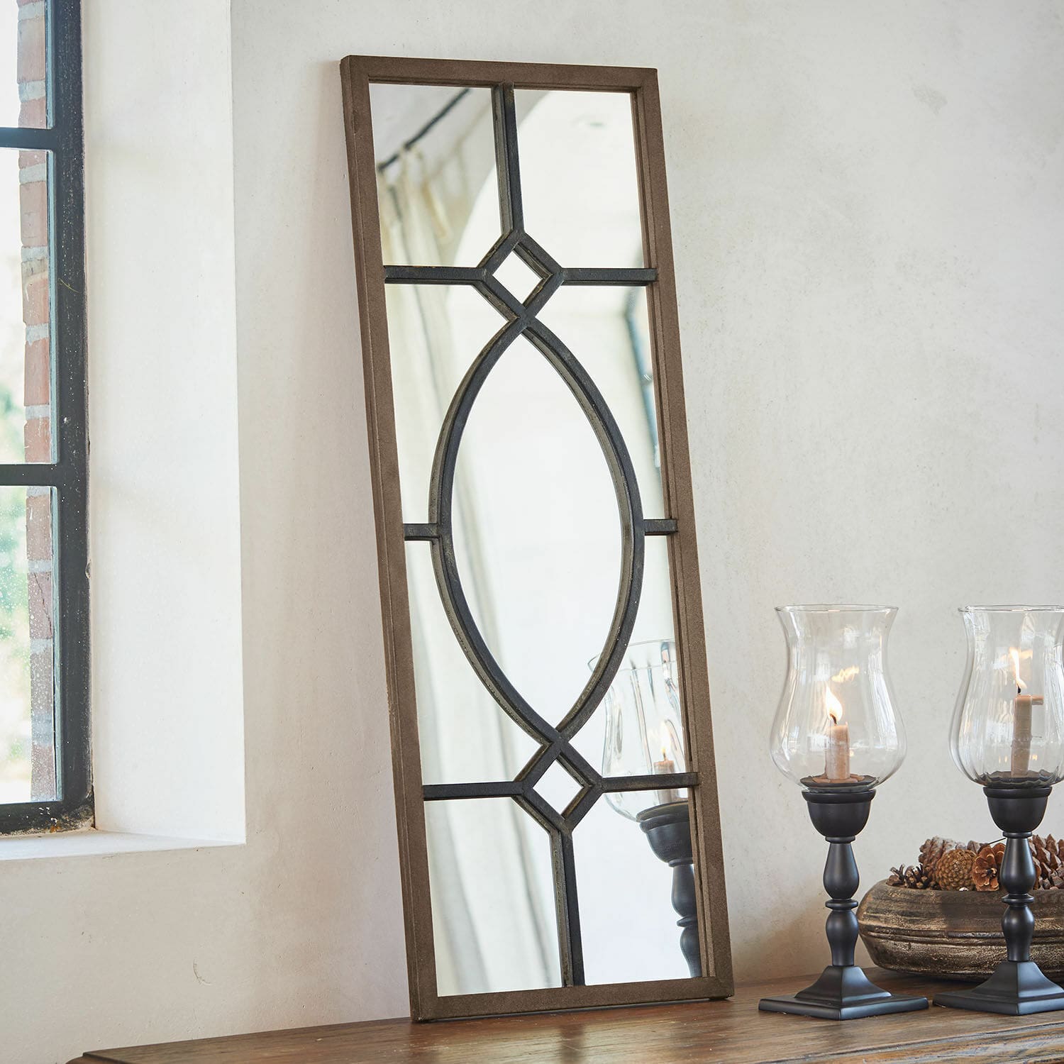 Espejo Millery Espejo rectangular con marco de madera marrón y diseño metálico negro sobre mesa con faroles