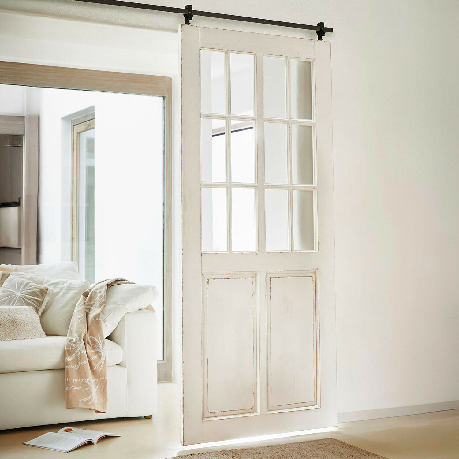 Puerta corredera de madera blanca con paneles de cristal en salón moderno y luminoso