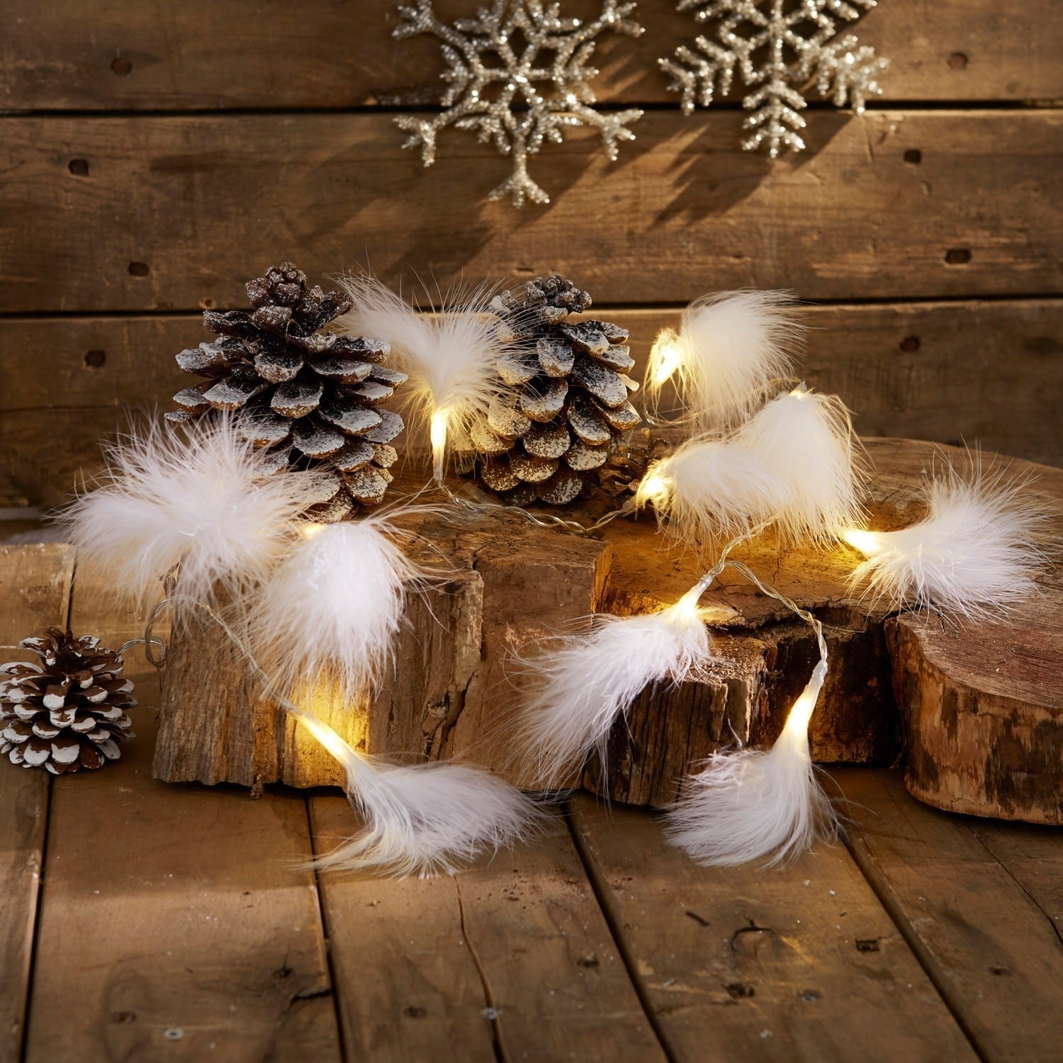 Set de 2 luces de hadas Forres Guirnalda de luces con plumas blancas sobre fondo de madera con piñas y decoración invernal