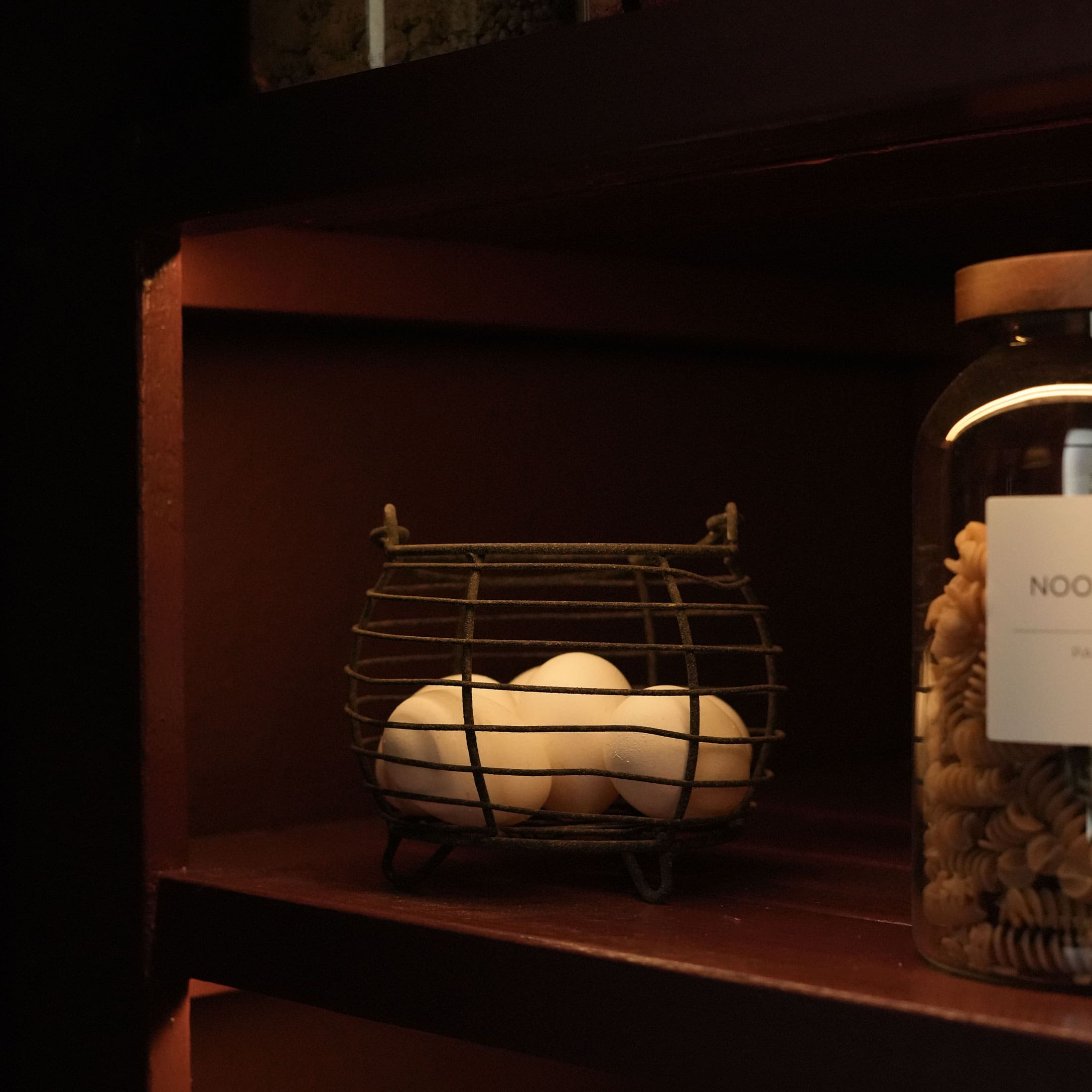 Cesta de metal con huevos blancos en estante de madera oscura en interior rústico