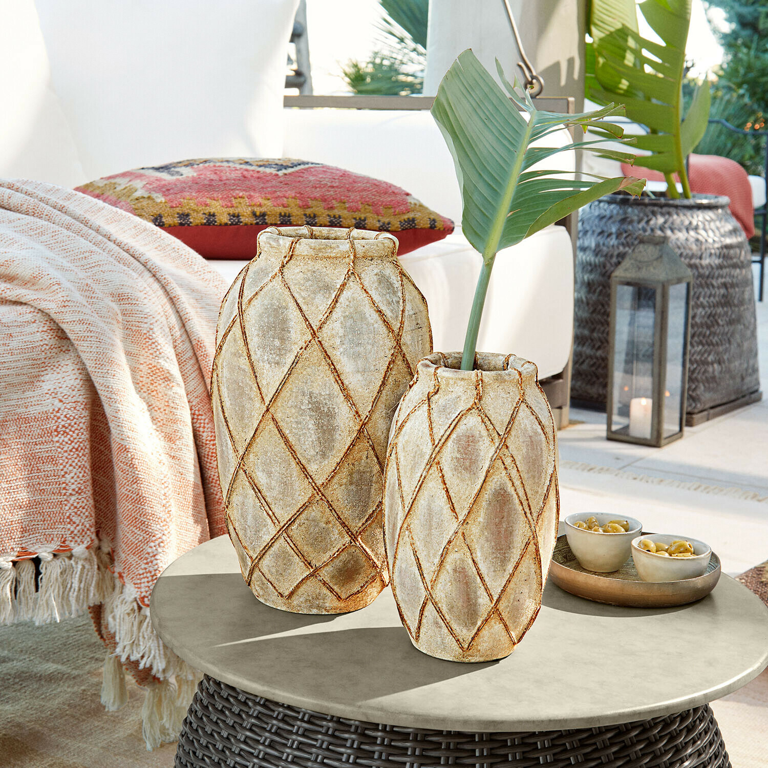 Set de 2 jarrones Deloriva Dos jarrones de cerámica beige con diseño geométrico sobre mesa de ratán en terraza