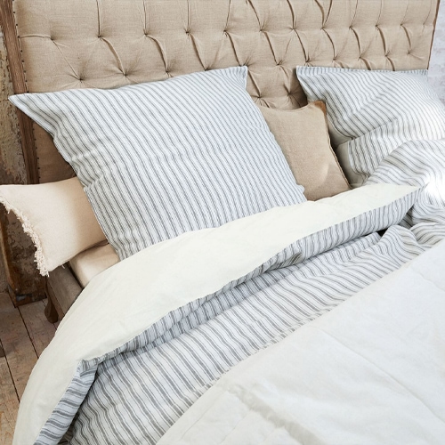 Ropa de cama de algodón con rayas grises sobre cabecero beige acolchado, elegante y cómoda