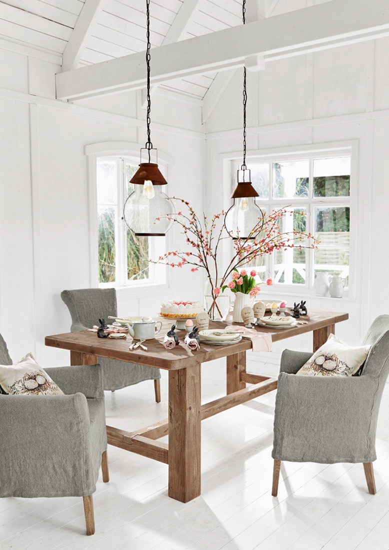 Comedor con mesa de madera maciza y sillas tapizadas grises en interior blanco luminoso