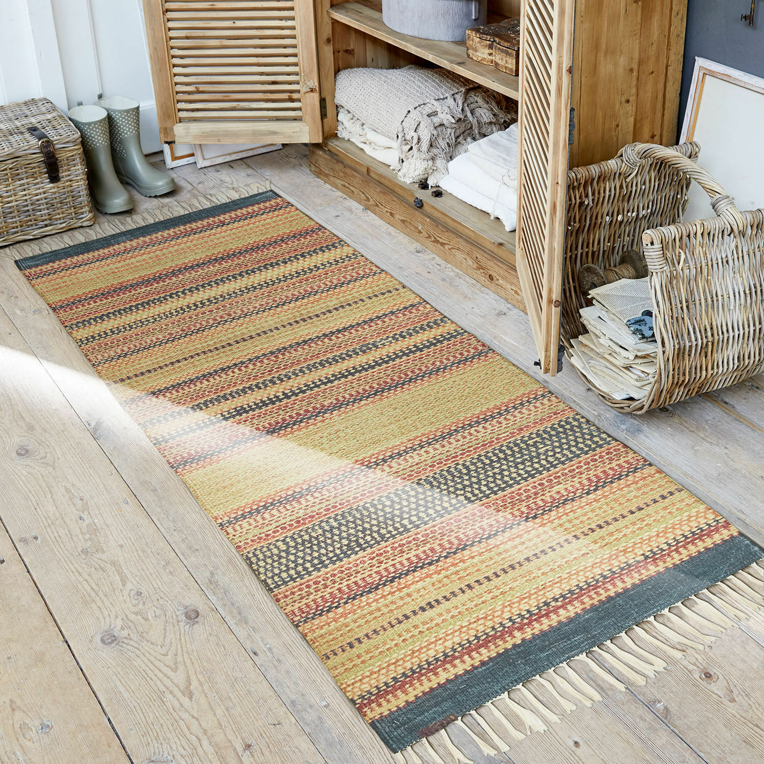 Alfombra para interior y exterior Atlanta Alfombra a rayas en tonos cálidos con flecos sobre suelo de madera en ambiente rústico