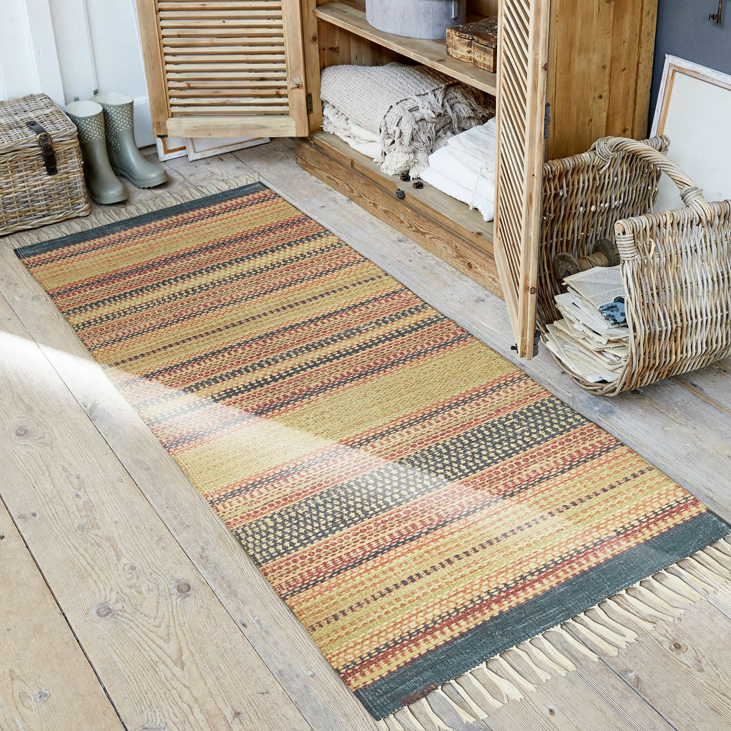 Alfombra para interior y exterior Atlanta Alfombra a rayas en tonos cálidos con flecos sobre suelo de madera en ambiente rústico