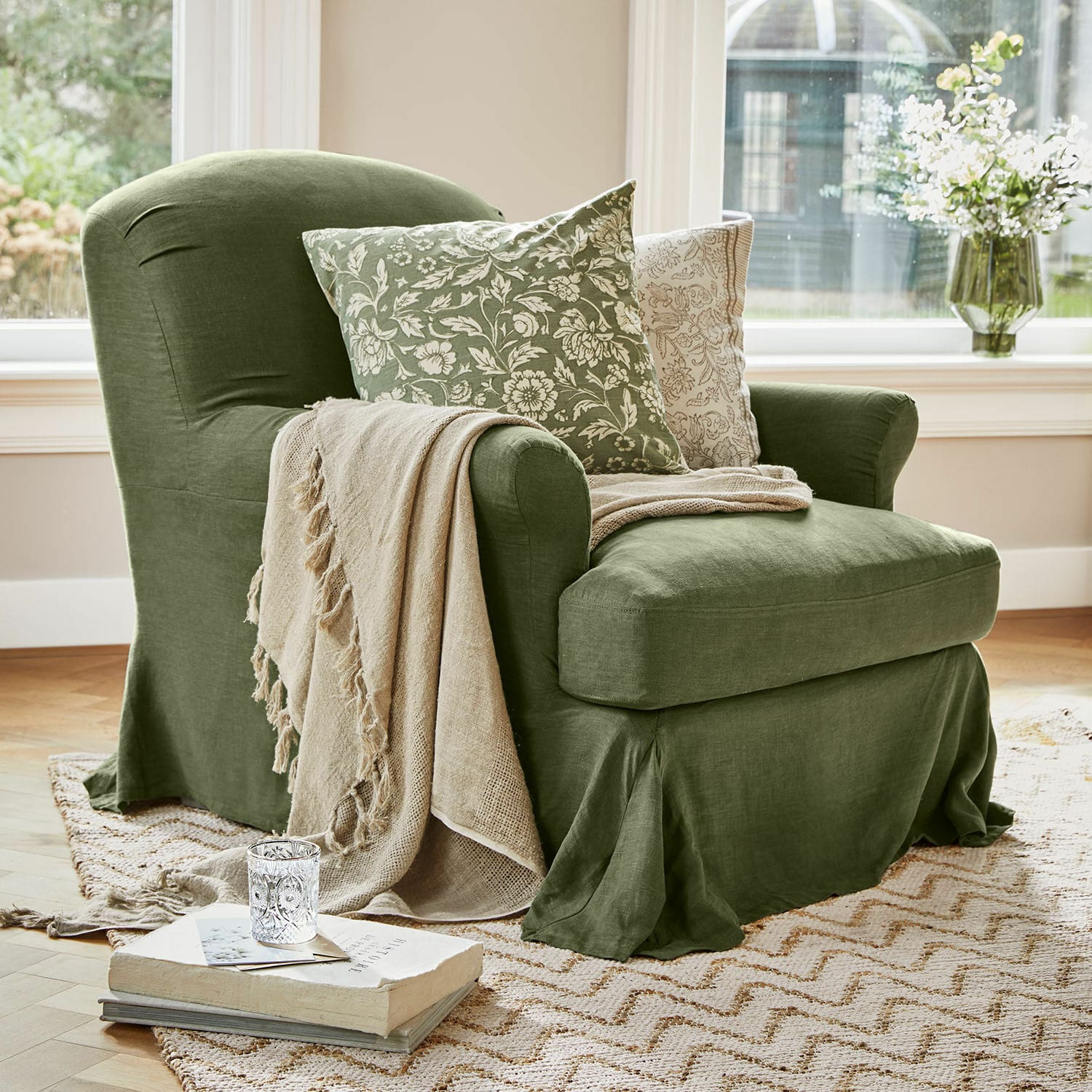 Sillón Vionnique Sillón verde de lino con manta beige y cojines con estampado floral sobre alfombra en sala