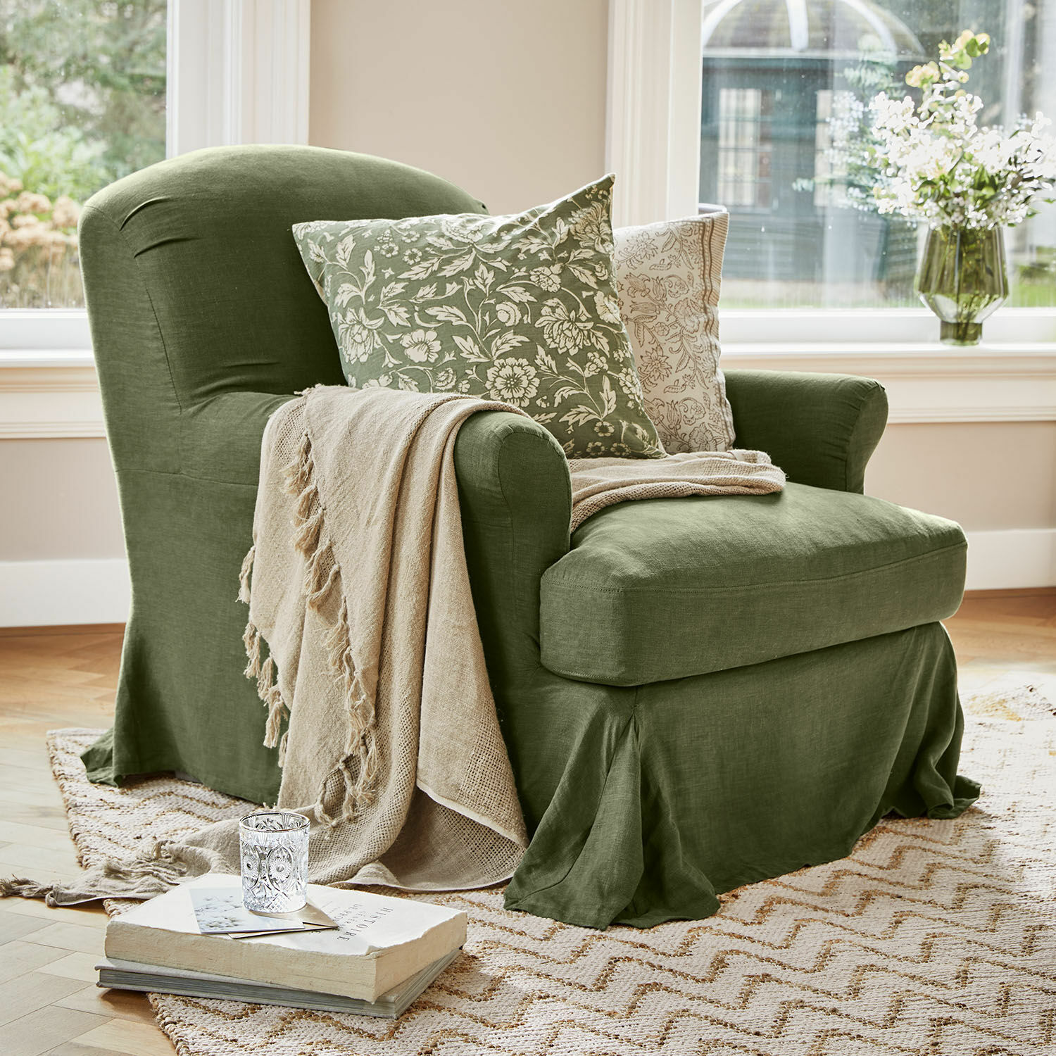 Sillón Vionnique Sillón verde de lino con manta beige y cojines con estampado floral sobre alfombra en sala